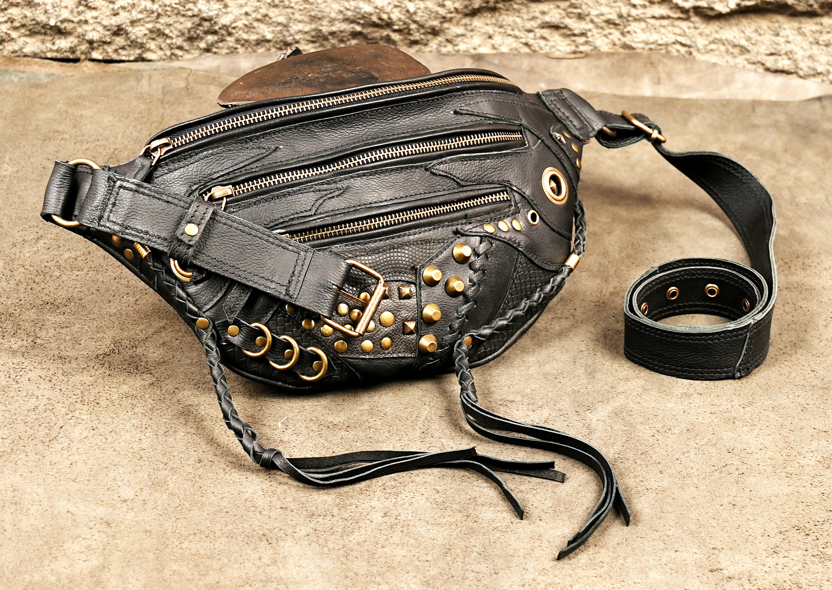 Boho-chic black leather fanny pack with braided leather tassels and decorative gold-tone hardware.