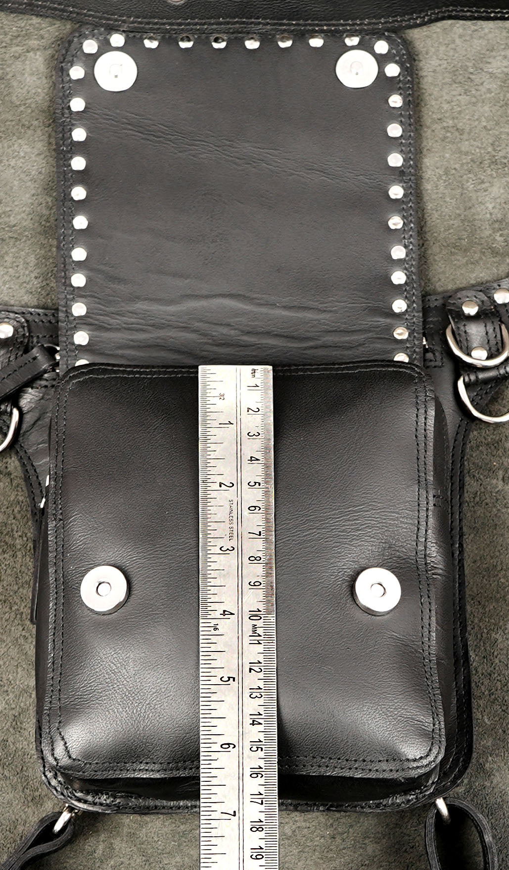 Edgy black leather hip bag with studded flap over textured background.