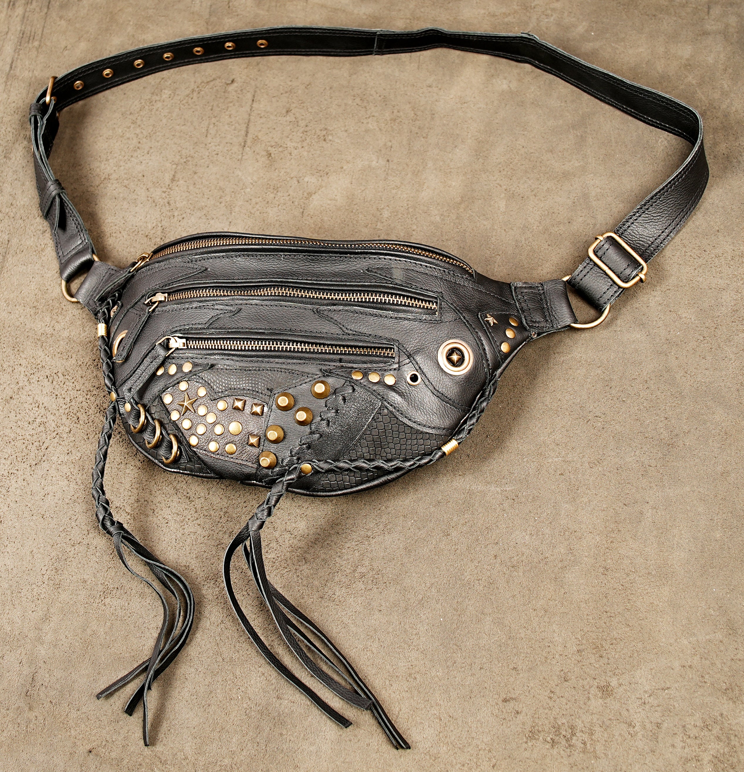 Distressed black leather waist bag with brass studs, star detailing, and braided fringe cords.
