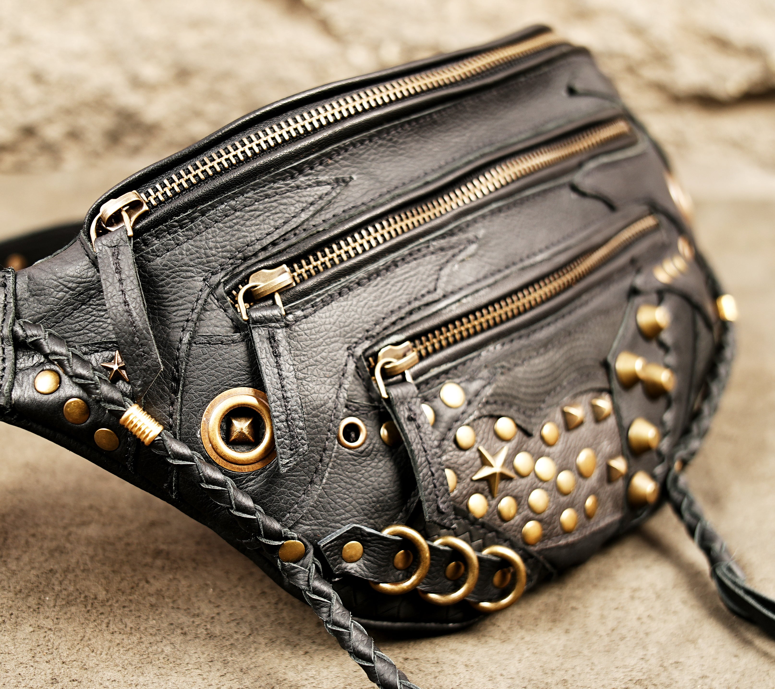 Edgy gothic black leather waist pack decorated with gold rivets and braided leather fringes.