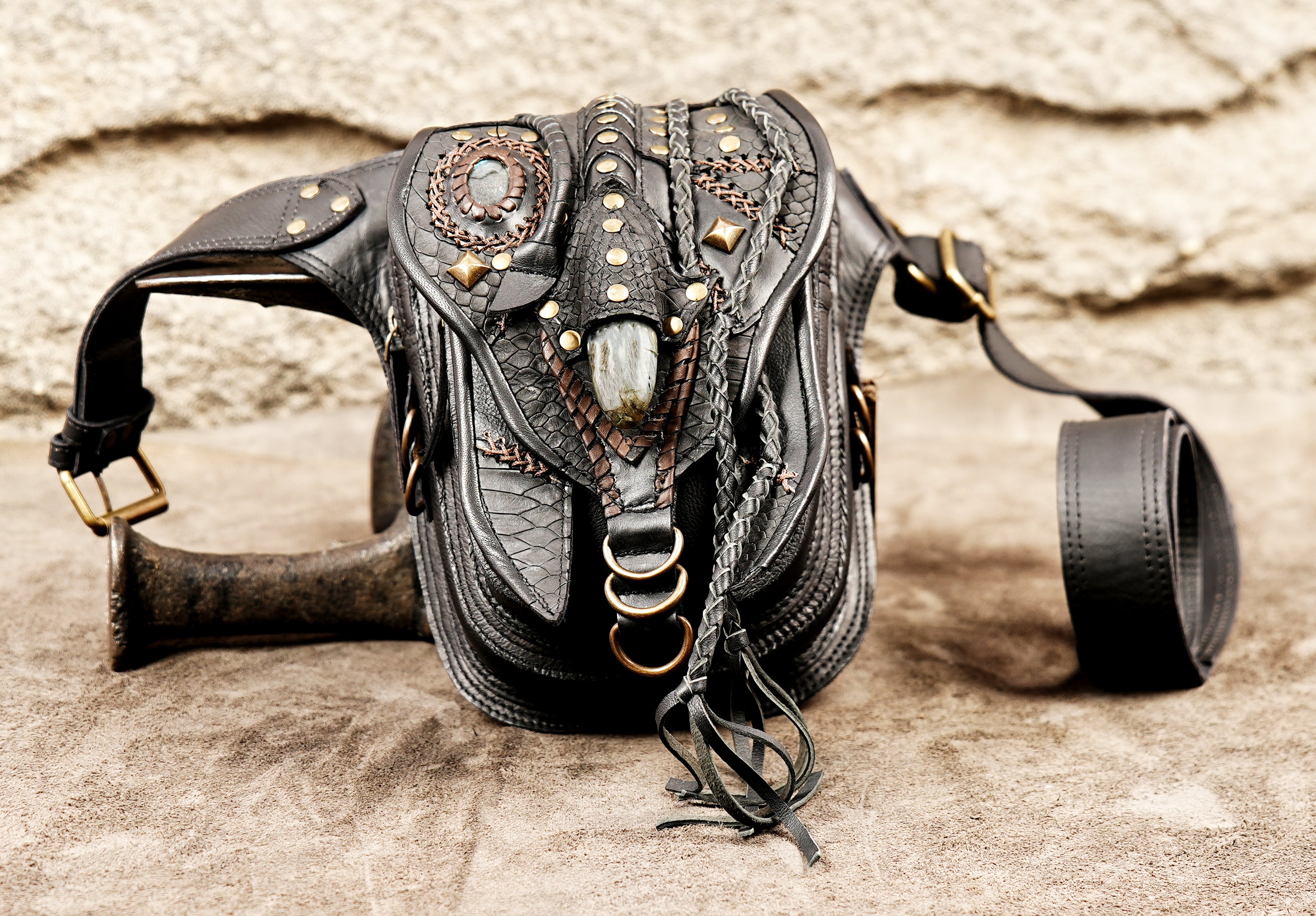 Punk style black leather thigh bag with decorative brass rivets and textured leather layering.