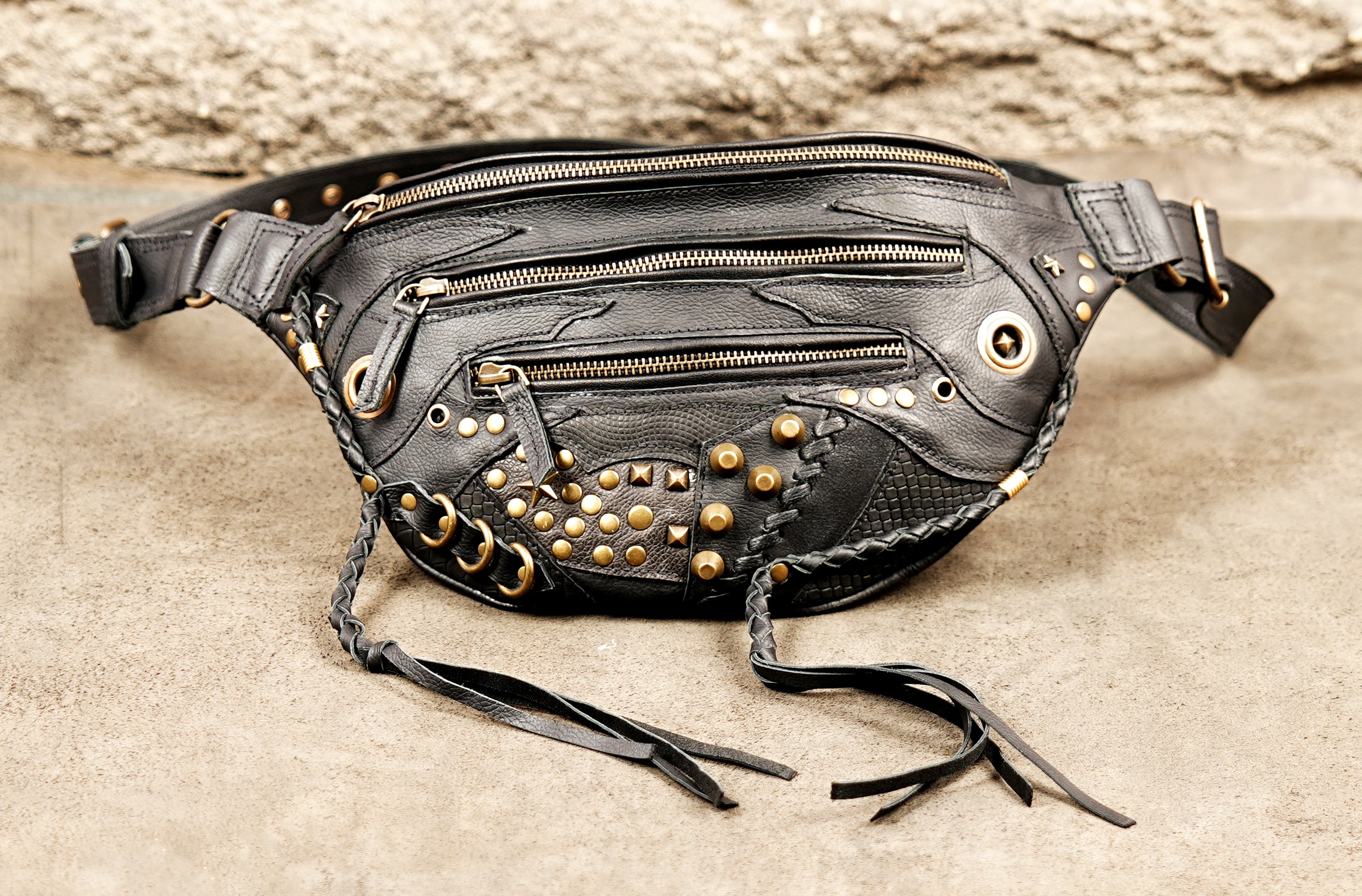 Durable black leather fanny pack with gold grommets, zippers, and fringed leather cords.