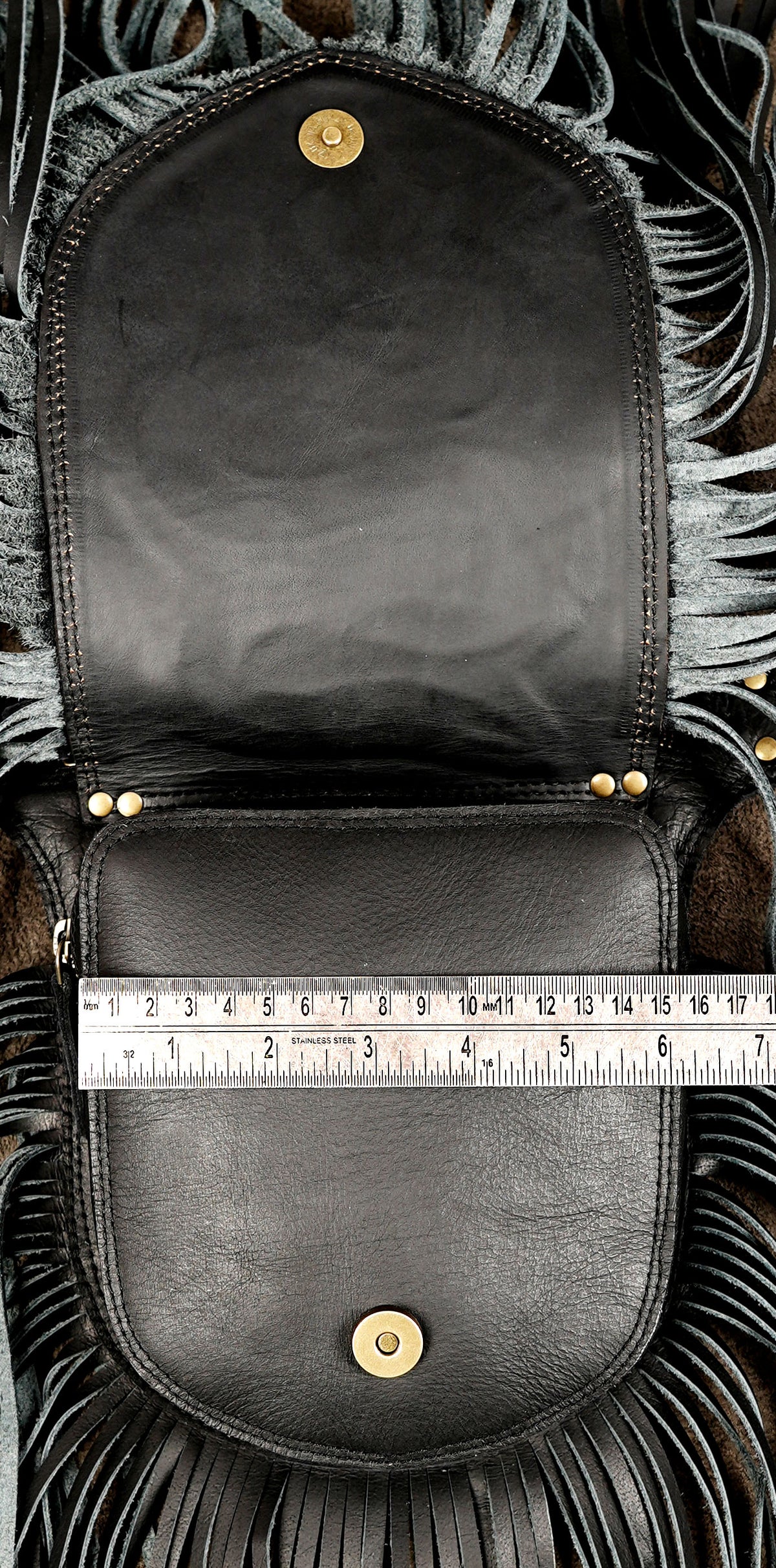 Black leather pouch bag with fringe trim and gold-tone hardware, shown open with a metal ruler across the front to indicate size.