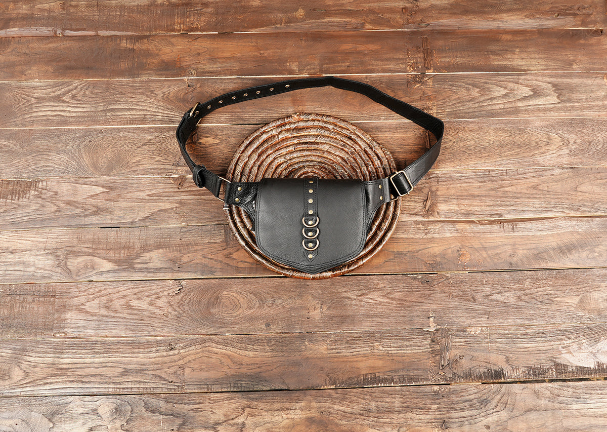 Black leather fanny pack resting on a rustic wooden table