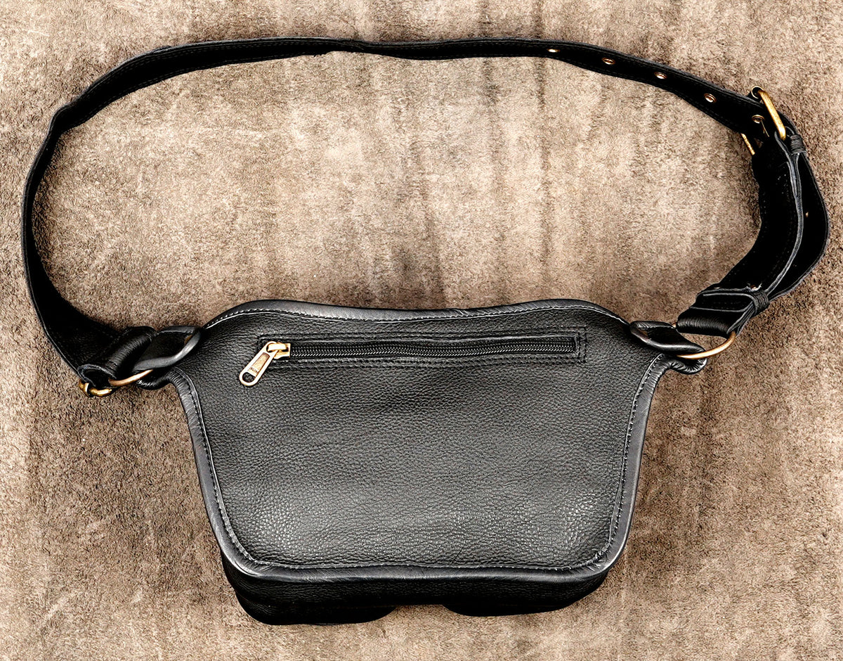 Black leather fanny pack with a wide adjustable strap and gold-tone hardware, laid flat on a textured brown background.