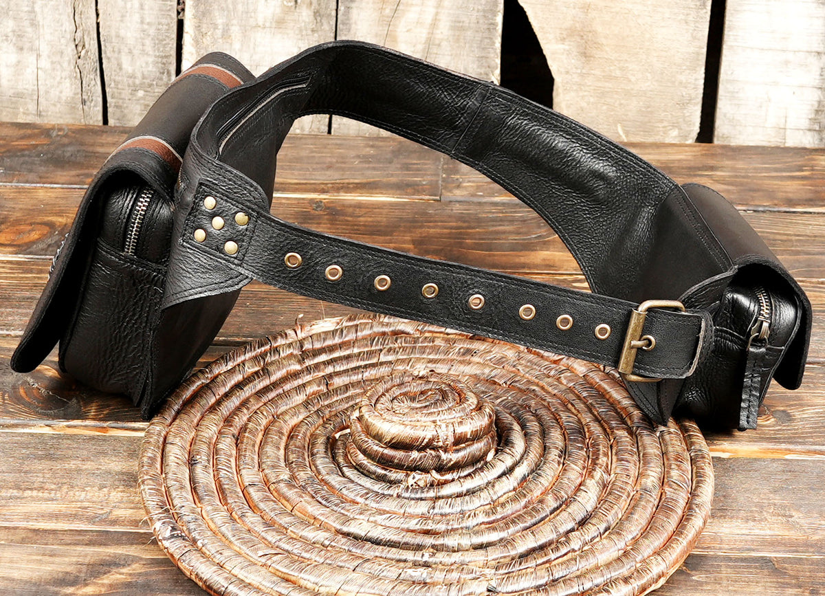 A black leather belt with brass-tone hardware and a zippered pouch, displayed on a rustic wooden surface.