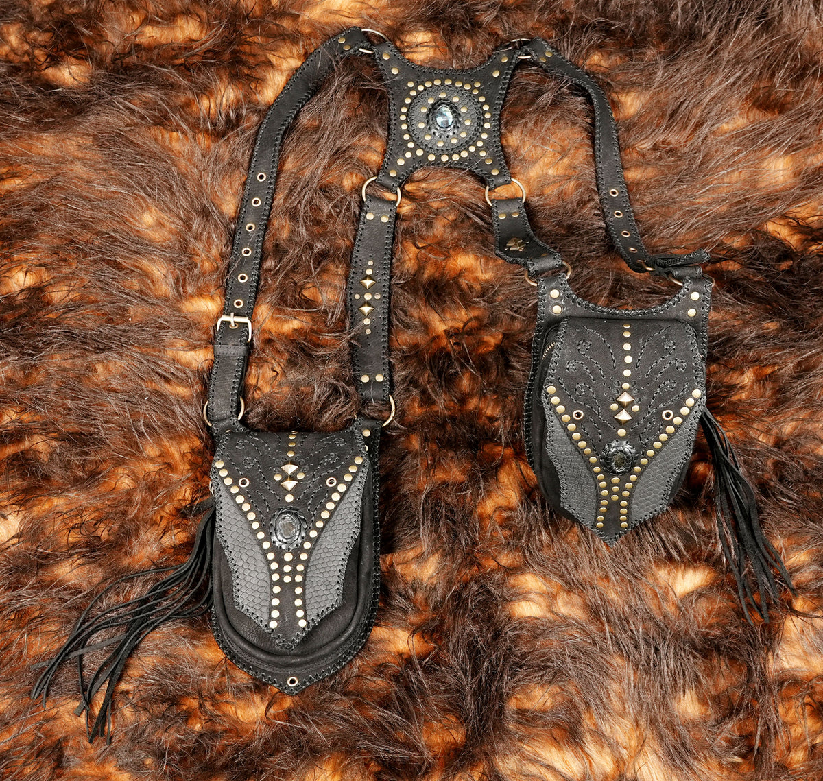 Gothic festival leather harness with dual thigh holsters, metallic studs, and hanging fringe.