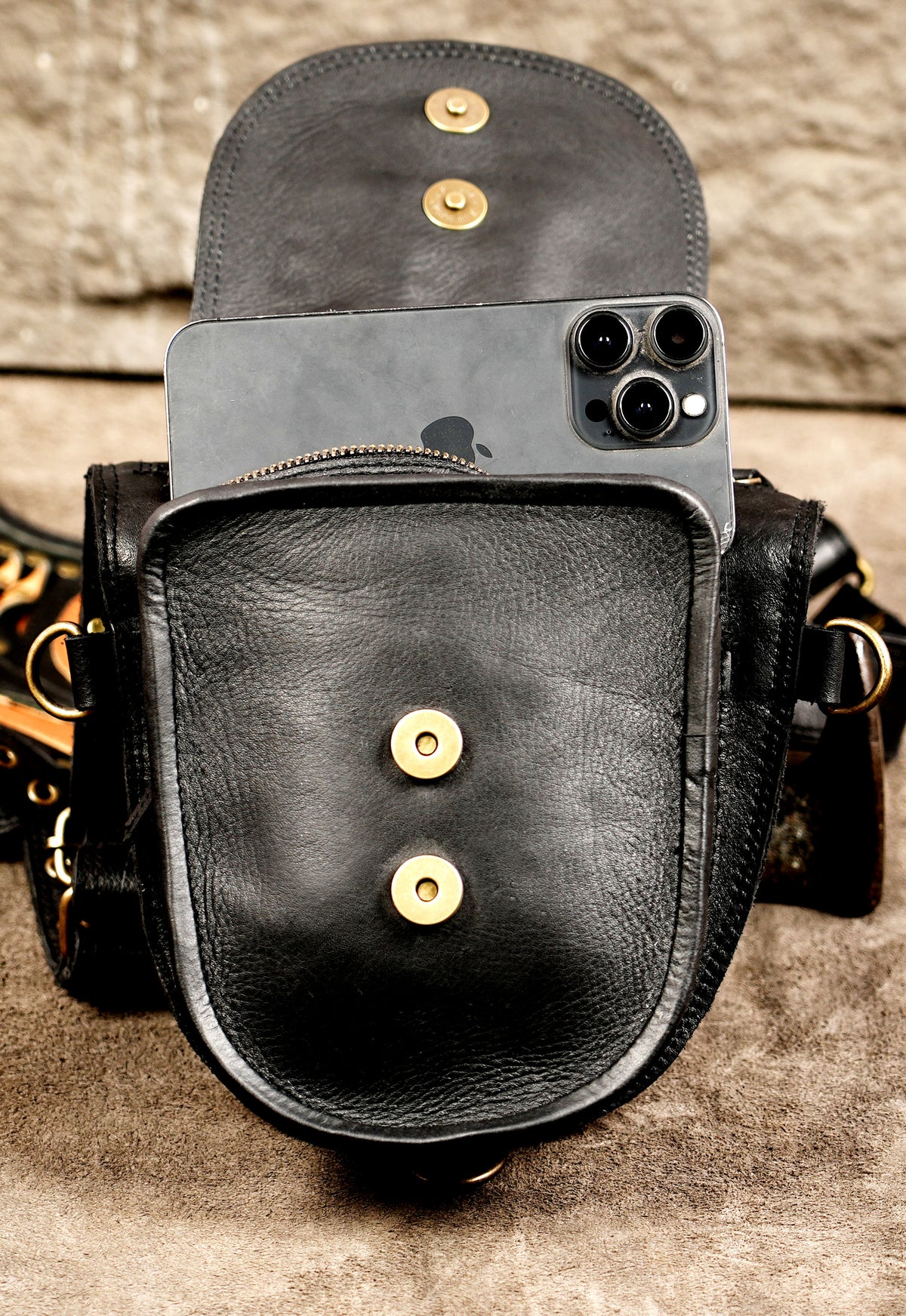 Black leather double pouch bag with shoulder harness, brass studs, and a central gemstone.