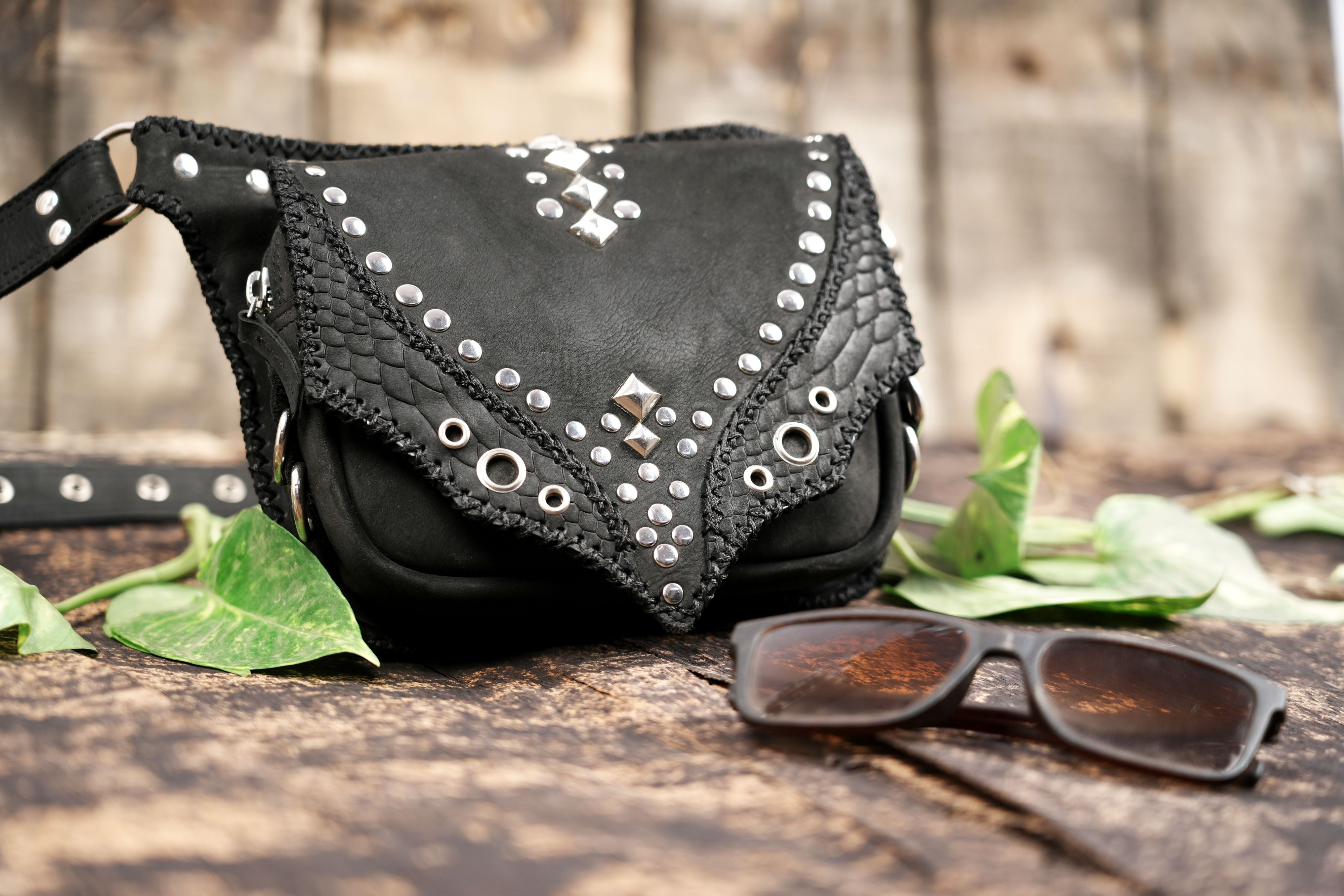 "Black leather belt pouch featuring rivets and layered textures"