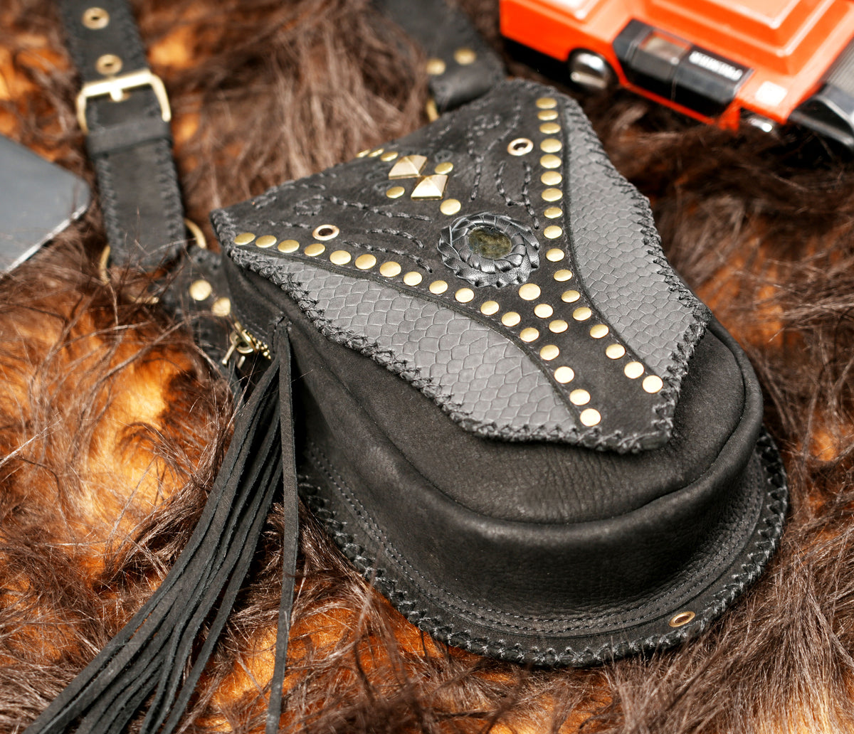 Handmade black leather thigh holsters with silver-tone studs and fringe for festival outfits.