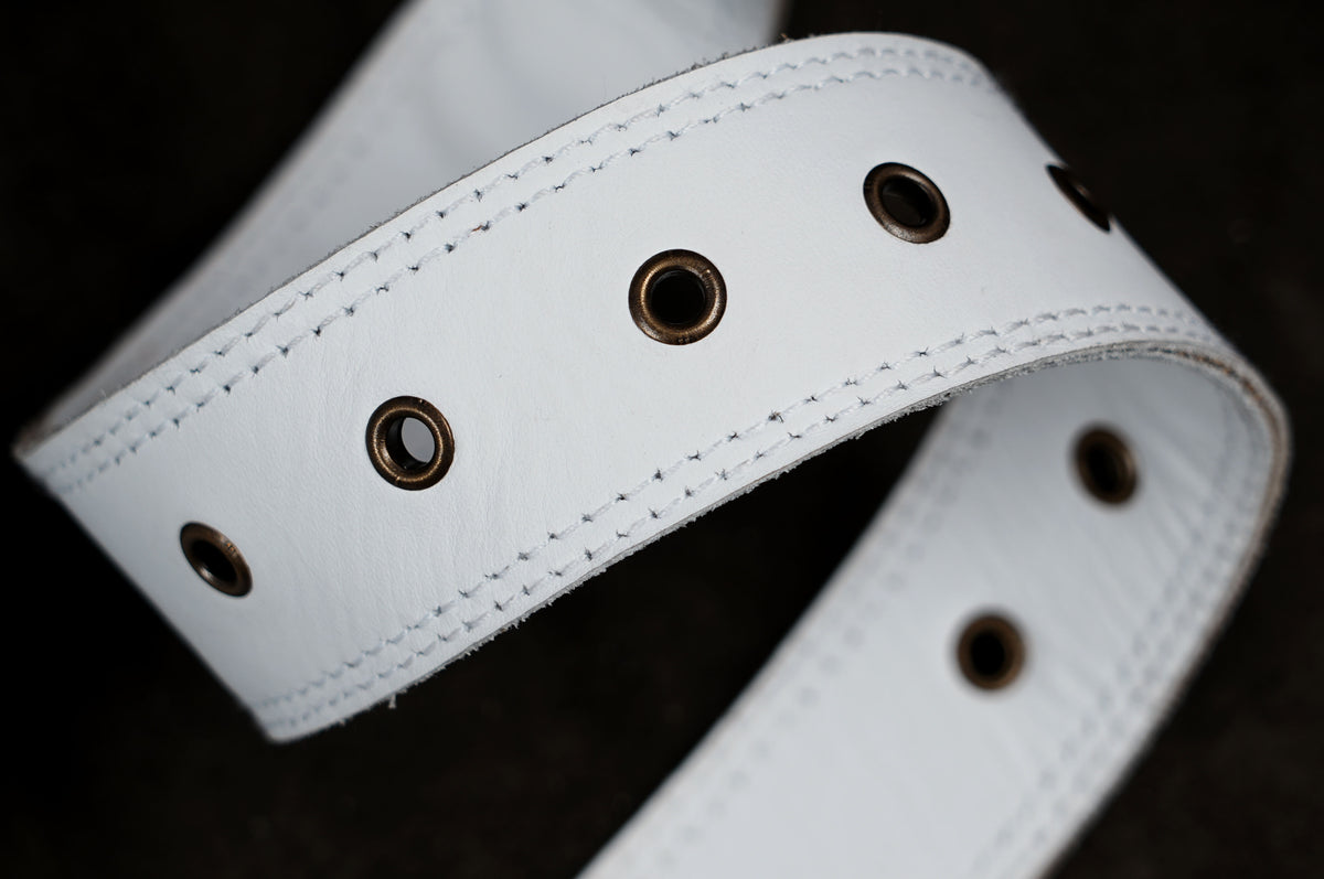 A close-up of a white leather belt with brass grommets, shown coiled against a dark background.