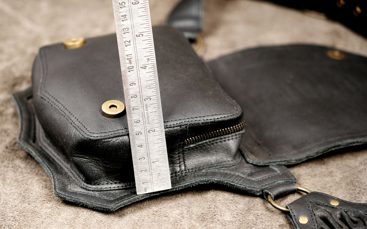 Close look at black leather belt bag with gathered front and brass studs