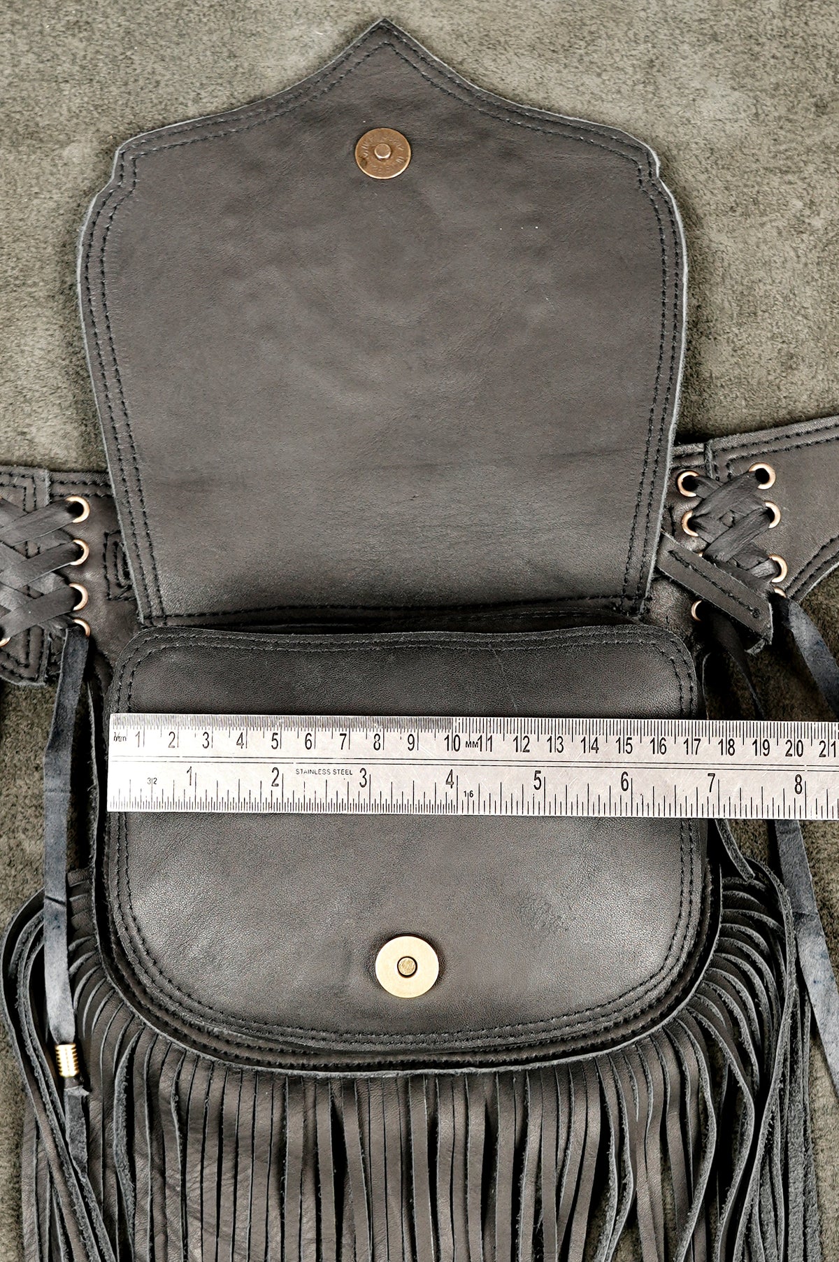 A black leather fringed pouch or small bag shown open, with a metal ruler placed across the front flap to indicate size. .