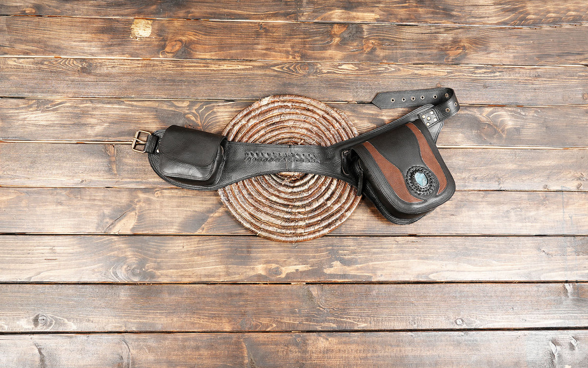 A black leather saddlebag-style pouch with brown leather trim and a circular brown-and-white coiled rope prop, photographed from above on a rustic wooden plank surface.