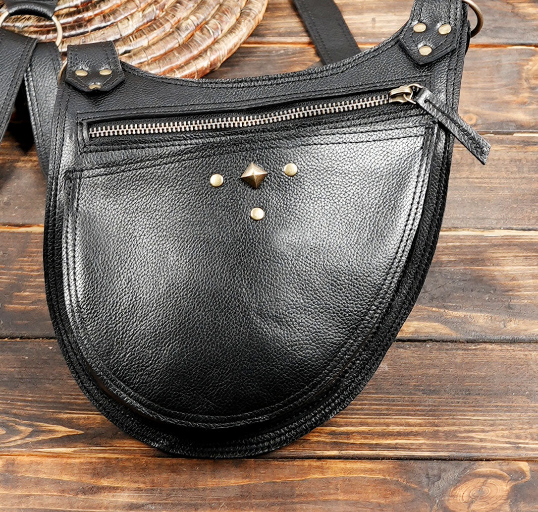 Handmade black leather double pocket harness bag with zipper closures and decorative brass hardware.