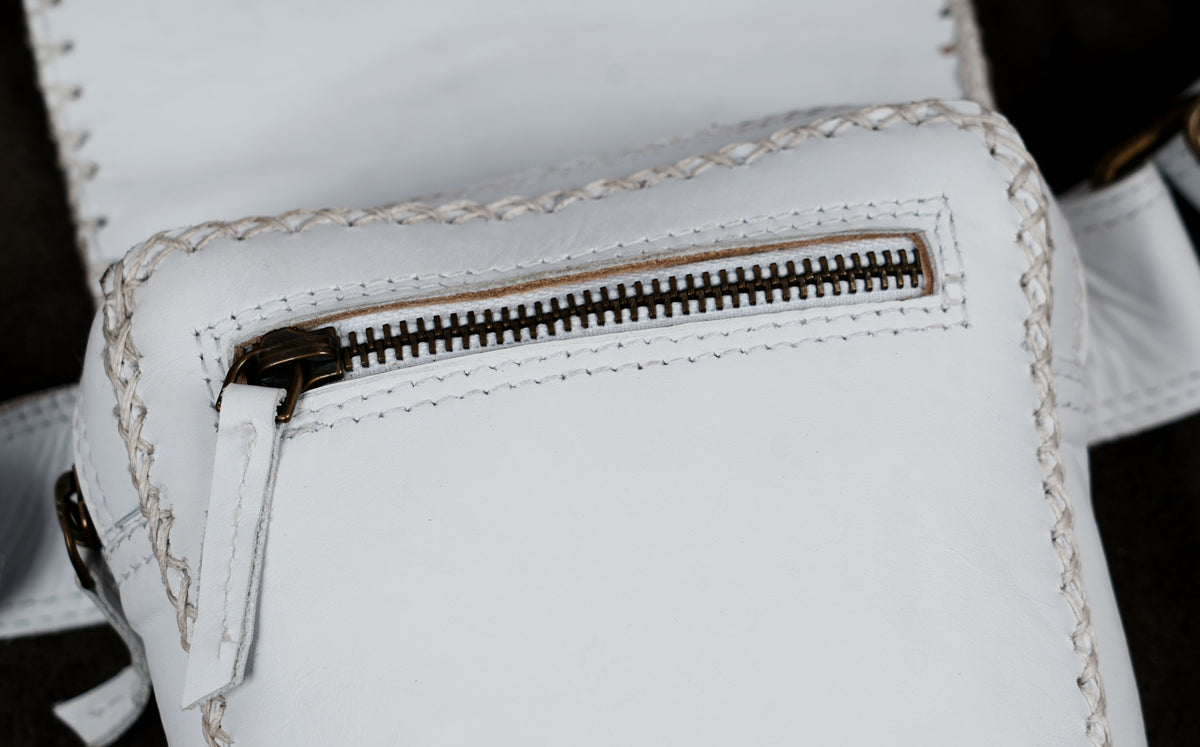 Close-up of a white leather bag featuring a zippered pocket with a dark metal zipper and decorative contrast stitching.