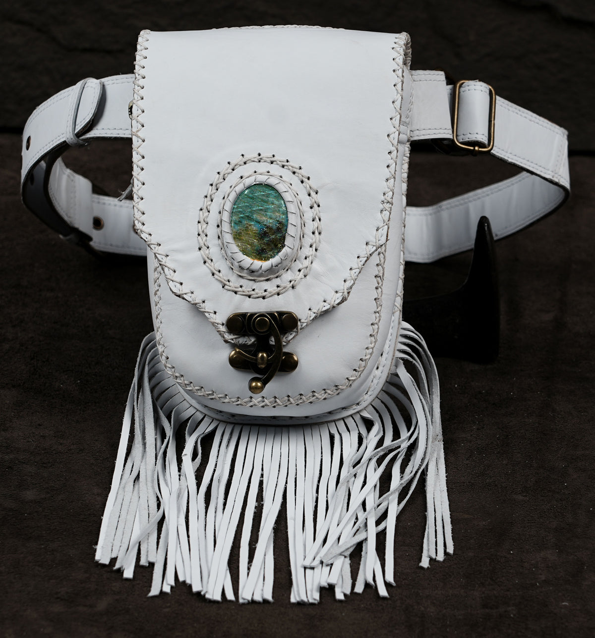A white leather fanny pack with a long fringe bottom, a central oval turquoise stone, and a decorative metal clasp.