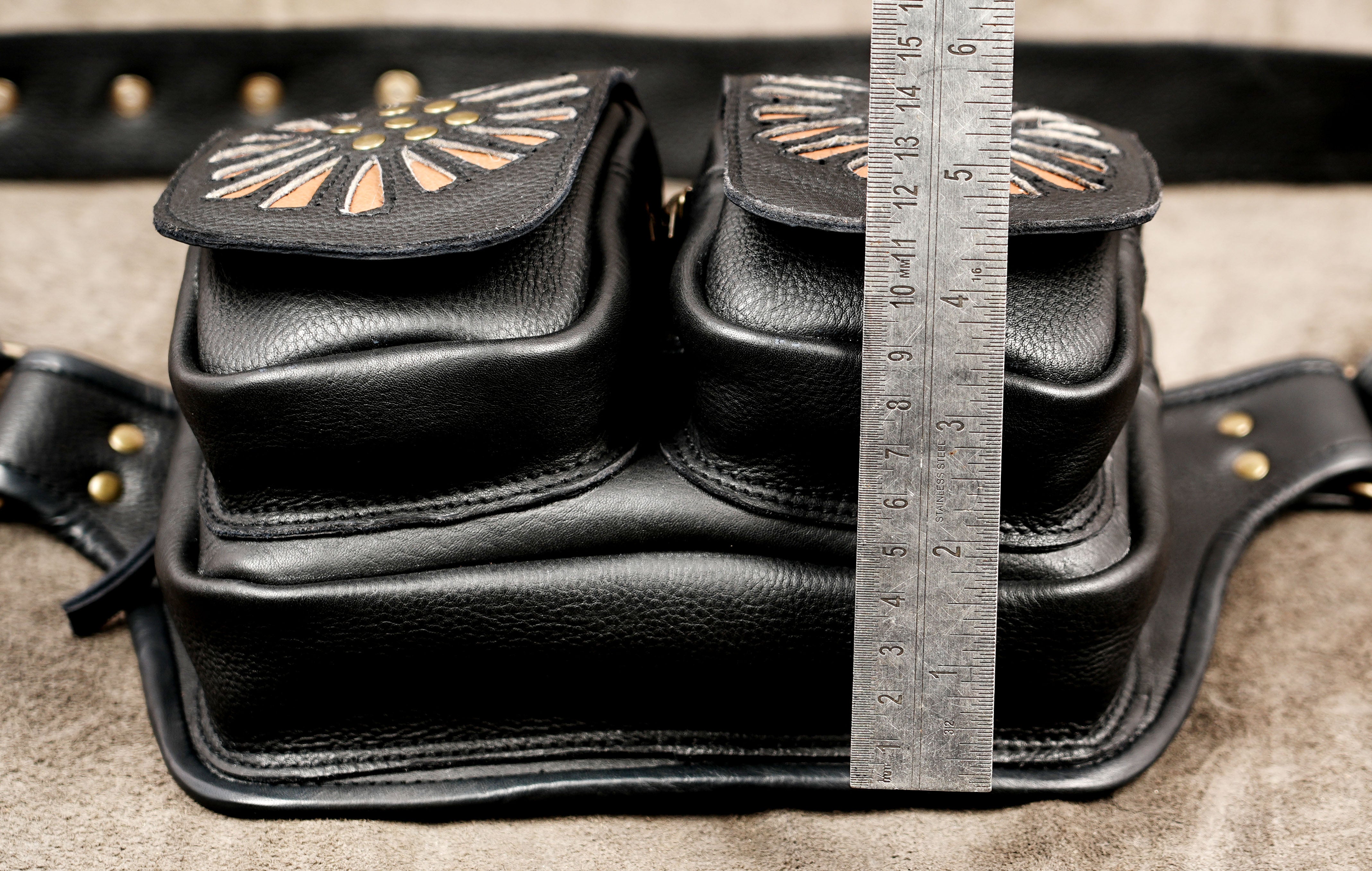Handcrafted black leather hip bag with tan sunburst flowers and brass rivets.