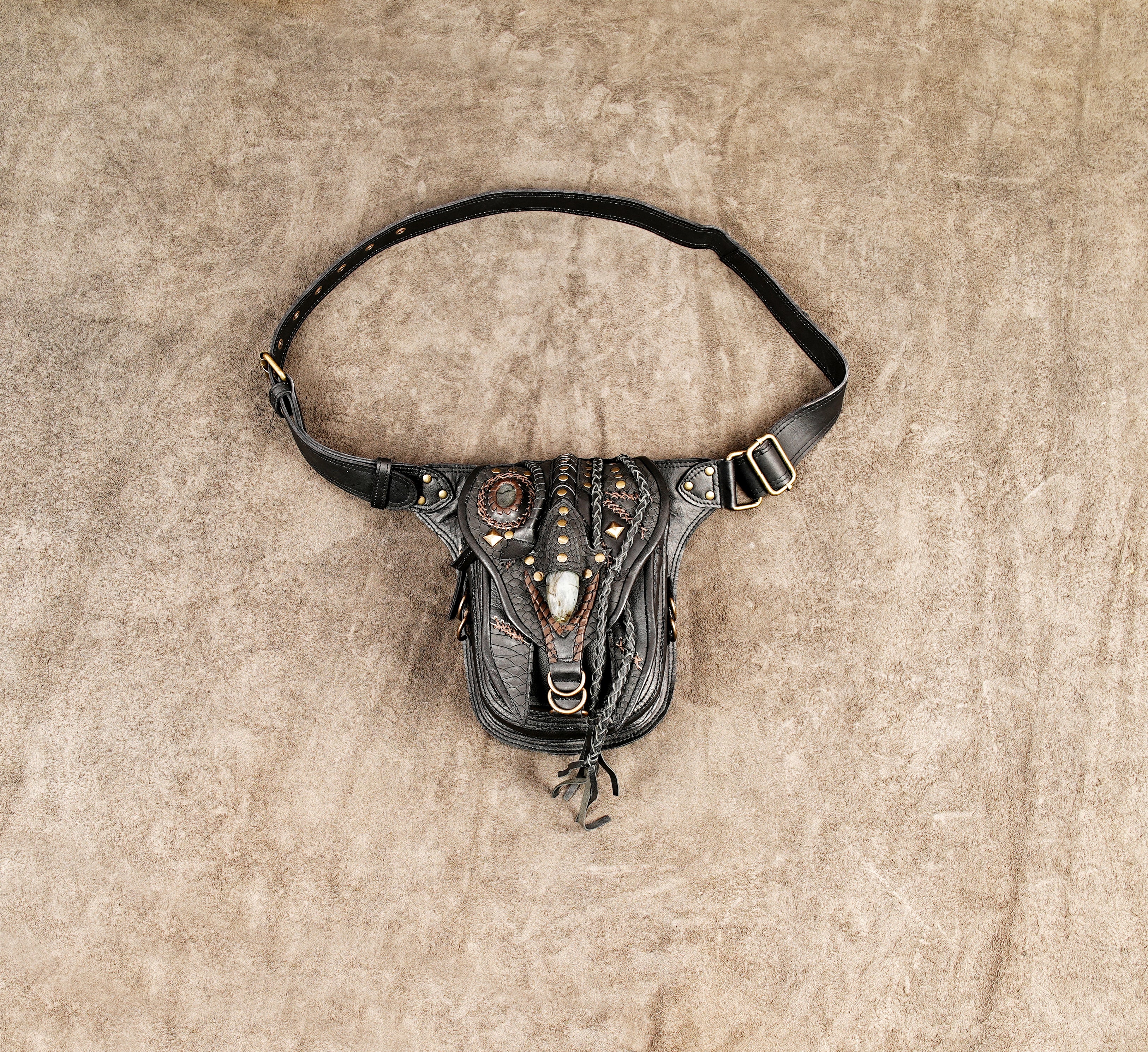 Black leather holster bag with intricate braided detailing and brass studs for festival outfits.