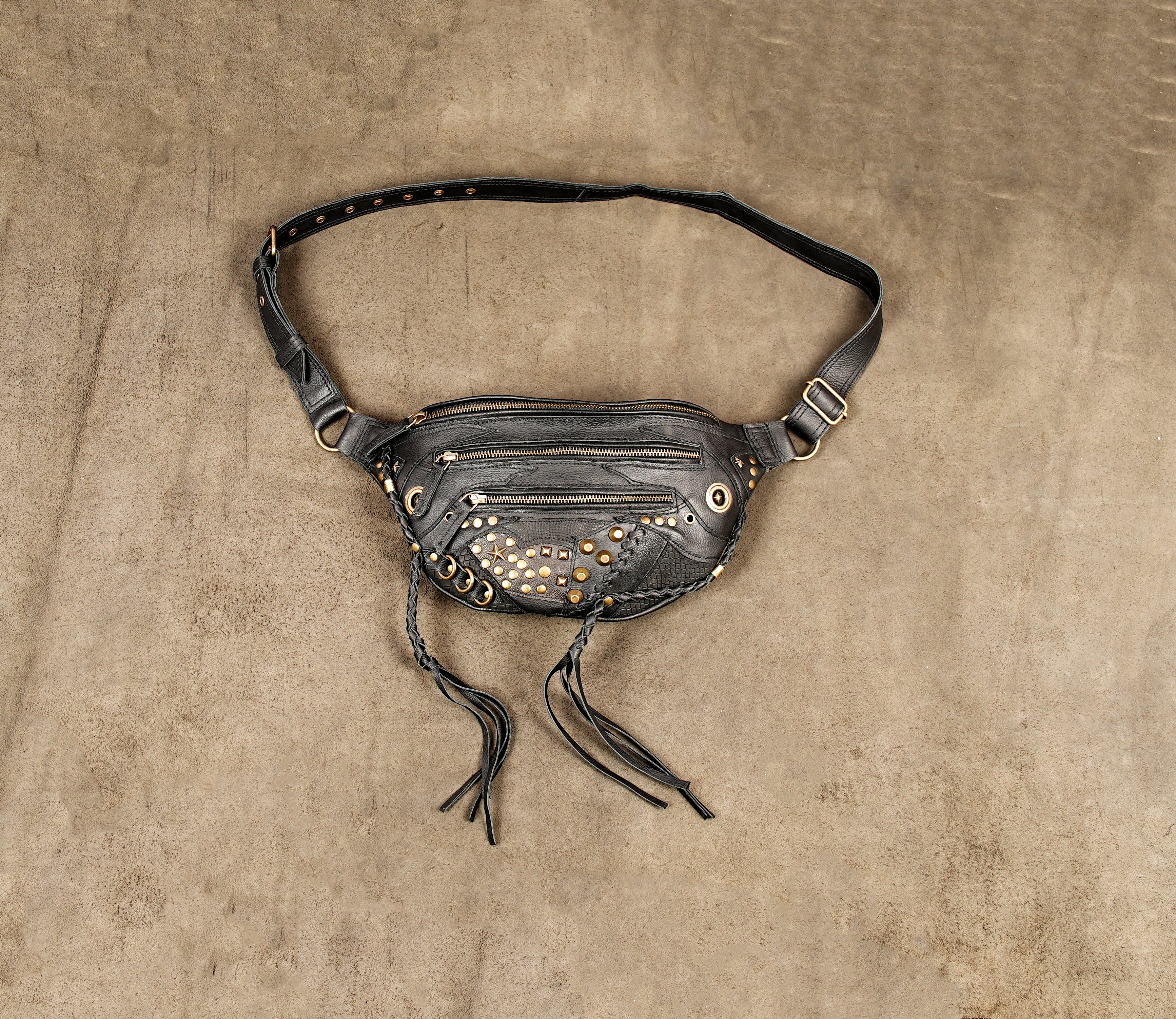 Black leather waist holster bag with gold studs and fringe tassels on a textured background.