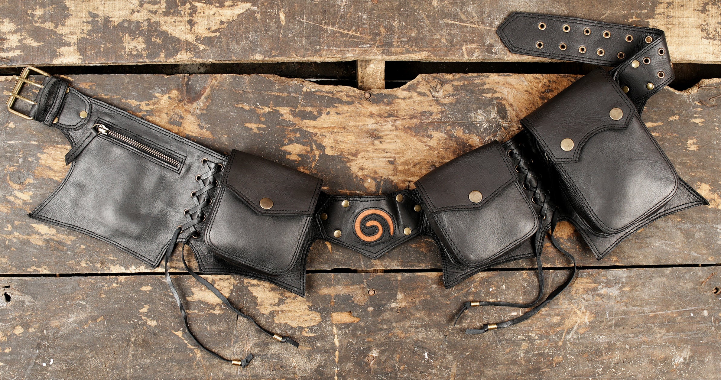 Black leather utility belt with multiple pouches, zipper pocket, and brass buckle on a rustic wooden background.