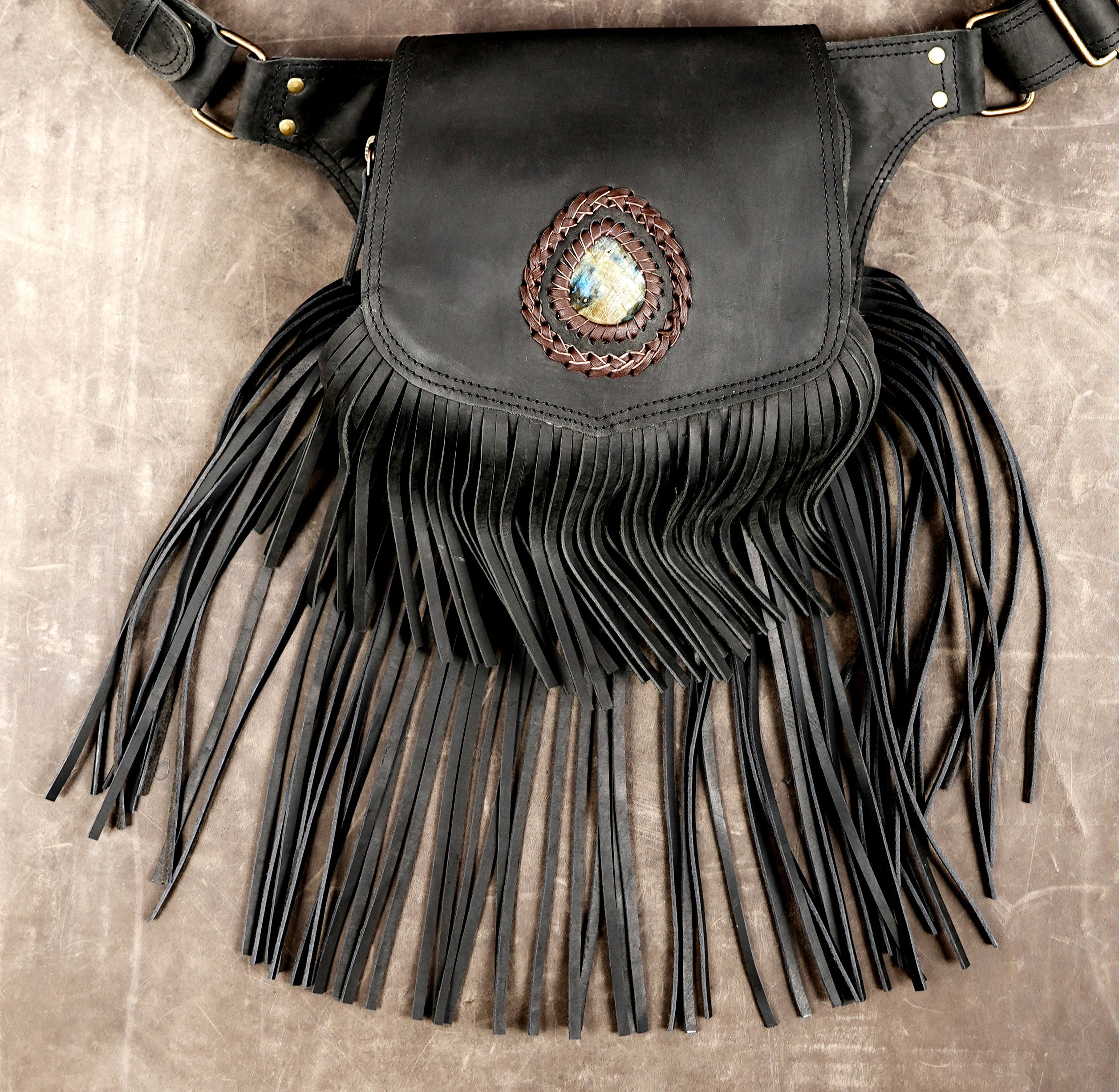 Black leather festival belt bag featuring long fringe and gemstone detail.
