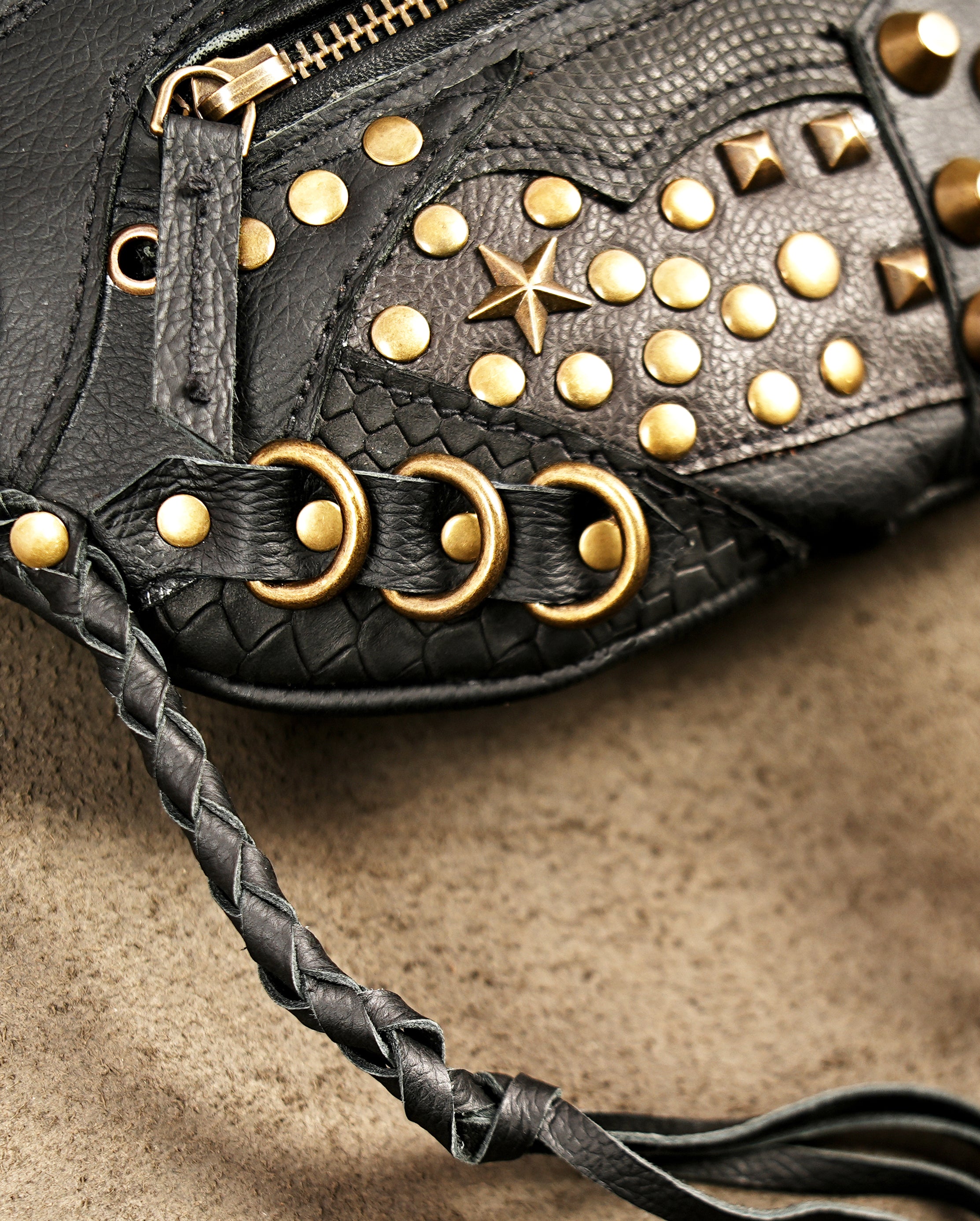 Close-up of black textured leather hip bag with gold star stud details.