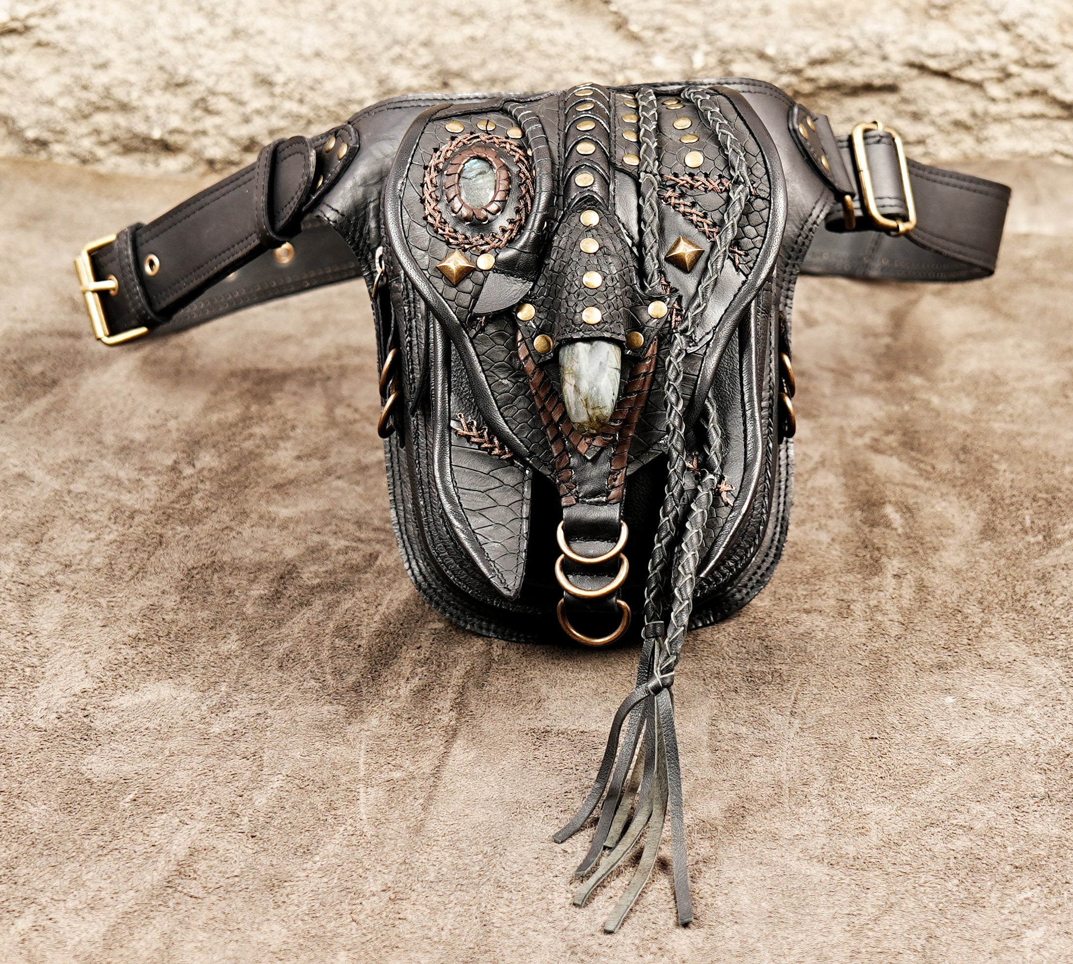 Bohemian festival thigh bag in black leather with braided tassels and ornate brass hardware.