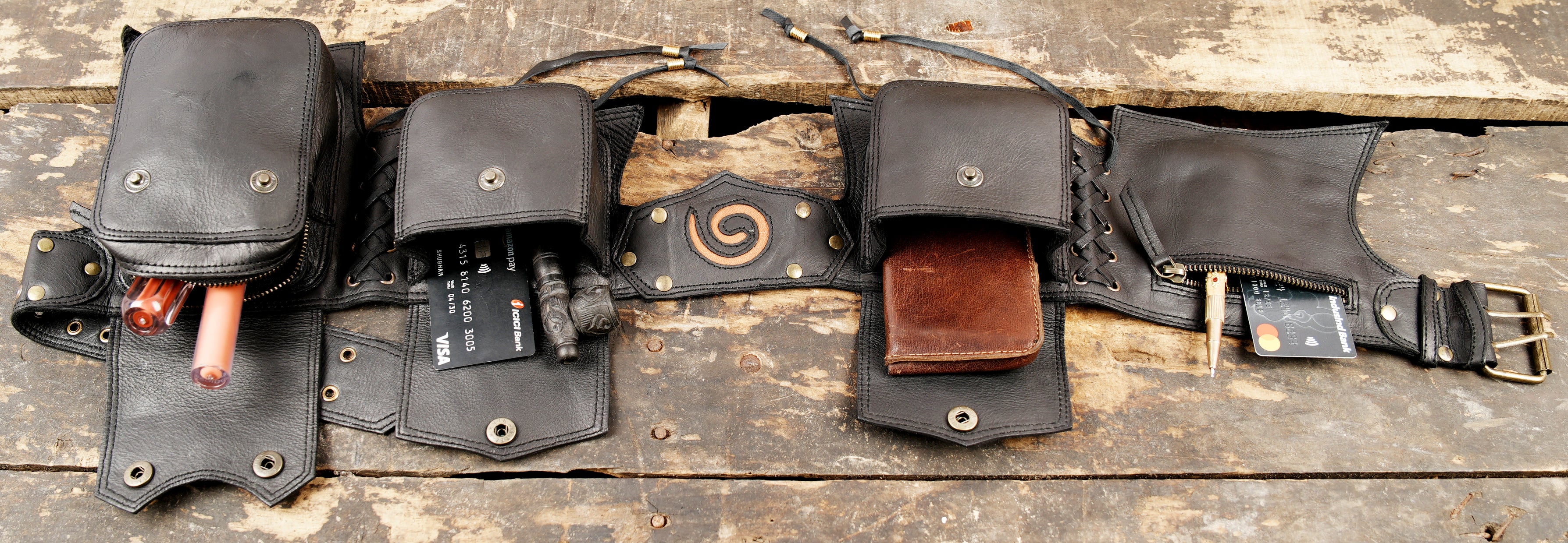Multi-pocket black leather utility belt with a center spiral emblem and adjustable double-prong buckle.