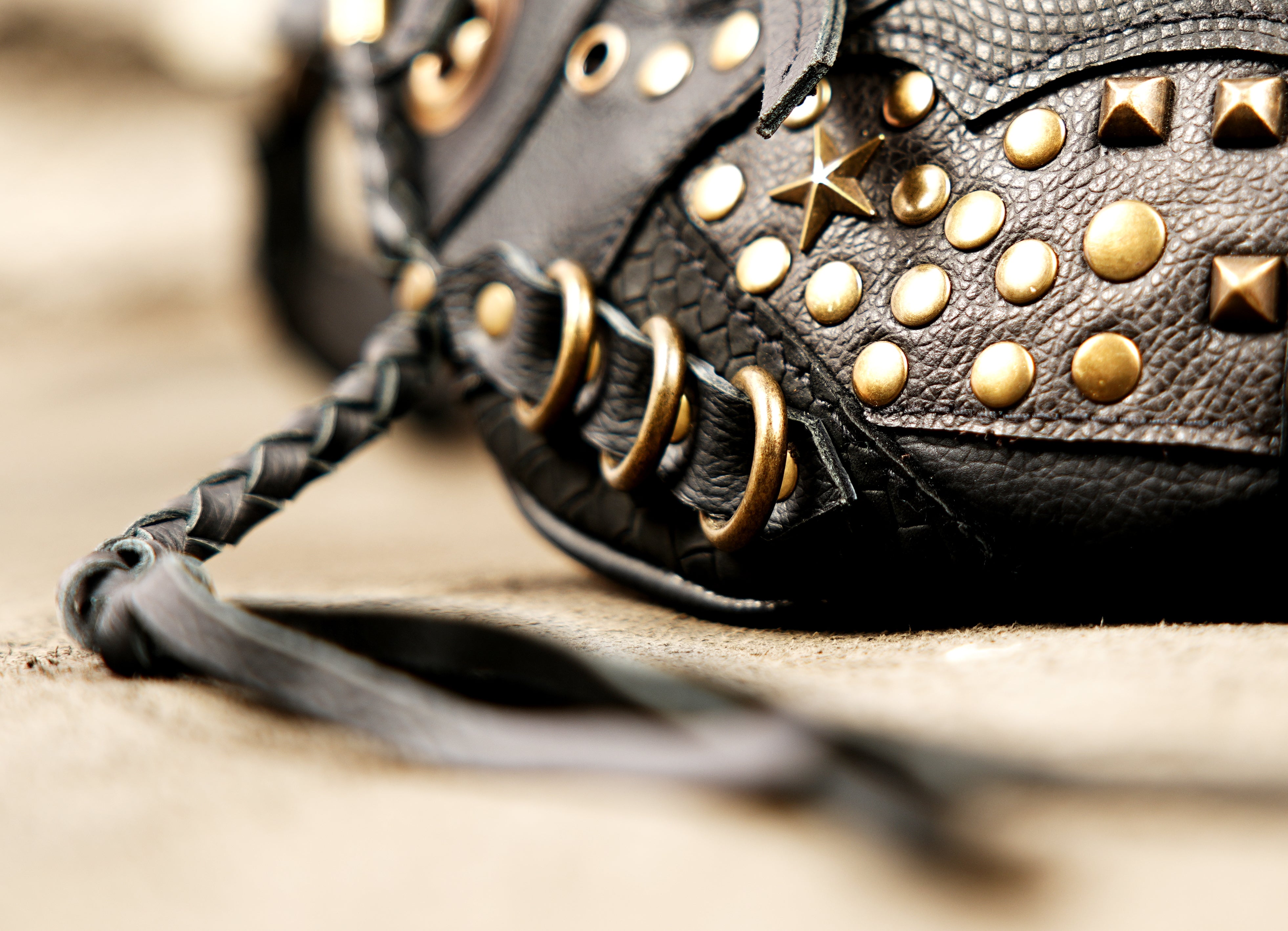 Vintage-inspired black leather fanny pack with gold-tone metal studs and braided fringe details.