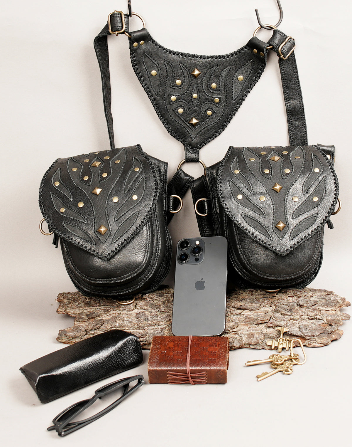 Black leather harness-style crossbody bag with two front pouches, studded and cutout leather detailing.