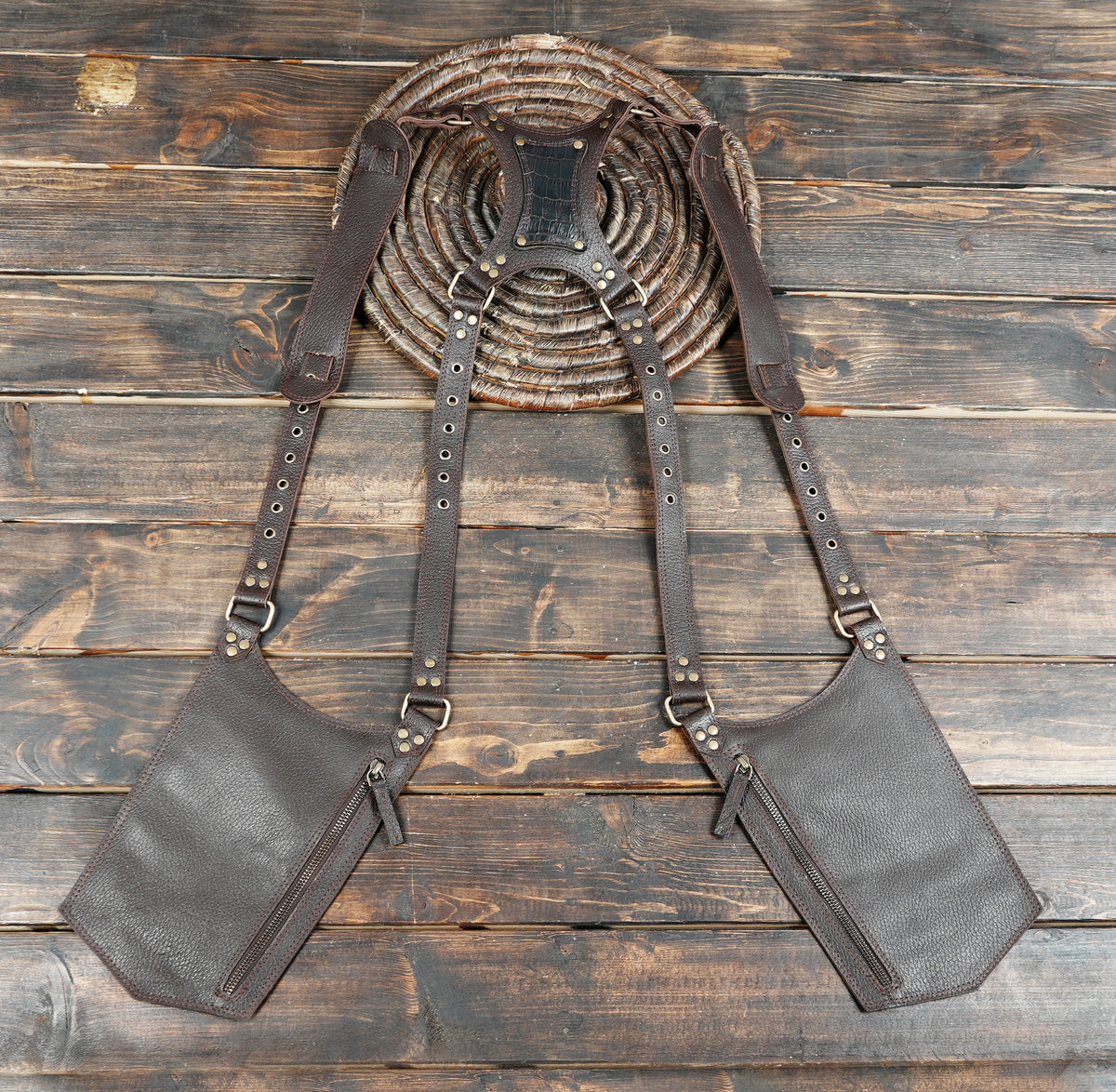 A dark brown leather harness-style bag with two large front zip pockets and adjustable shoulder straps.