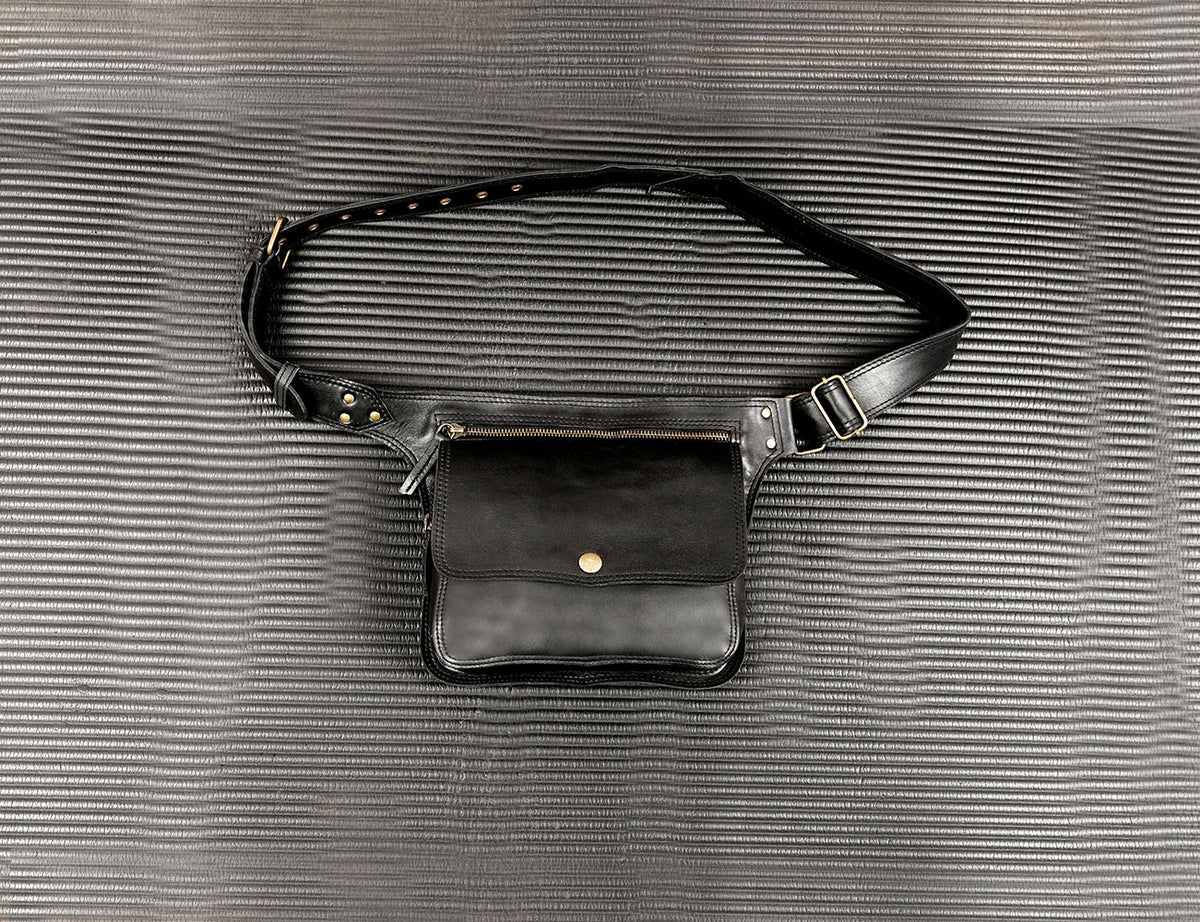 Black leather hip bag with adjustable belt strap on a textured grey background