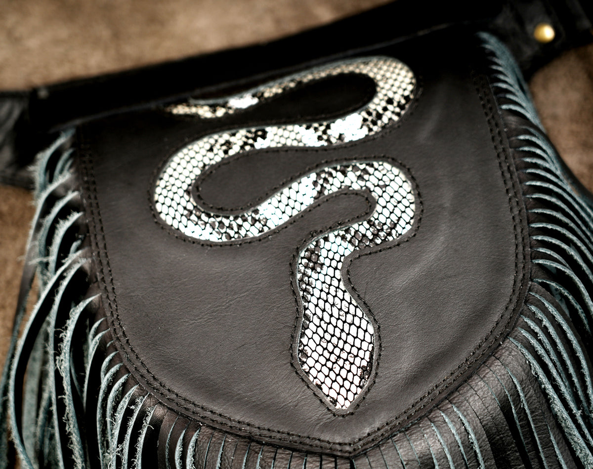 Close-up of a black leather fringed bag featuring a prominent white and black snakeskin-patterned patch on the front.
