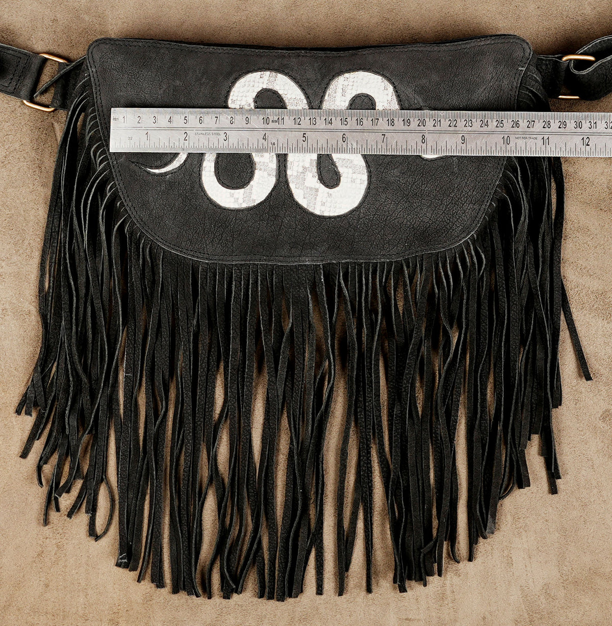 Black leather-look waist bag with white snake design and flowing fringe for women.