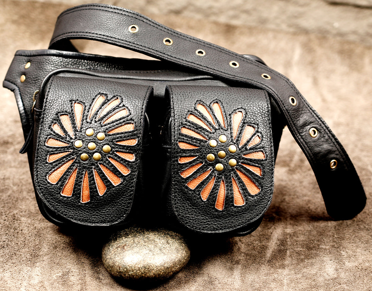Black leather shoulder bag with two front flap pockets featuring cutout sunburst designs in orange-brown and gold-tone studs .