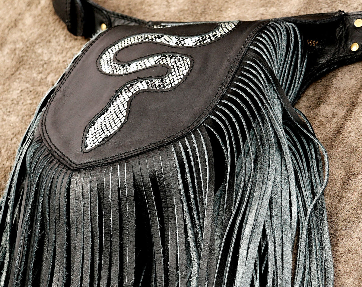 A close-up of a black leather fringe belt with a prominent black patch featuring a silver snake design.