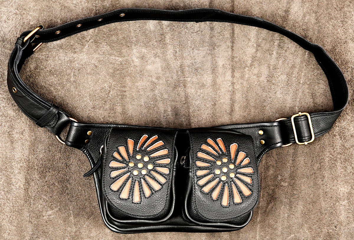 Black leather fanny pack with two large front pouches featuring cutout floral designs in black and tan, with a matching adjustable black leather belt and gold-tone hardware, laid flat on a textured brown surface.