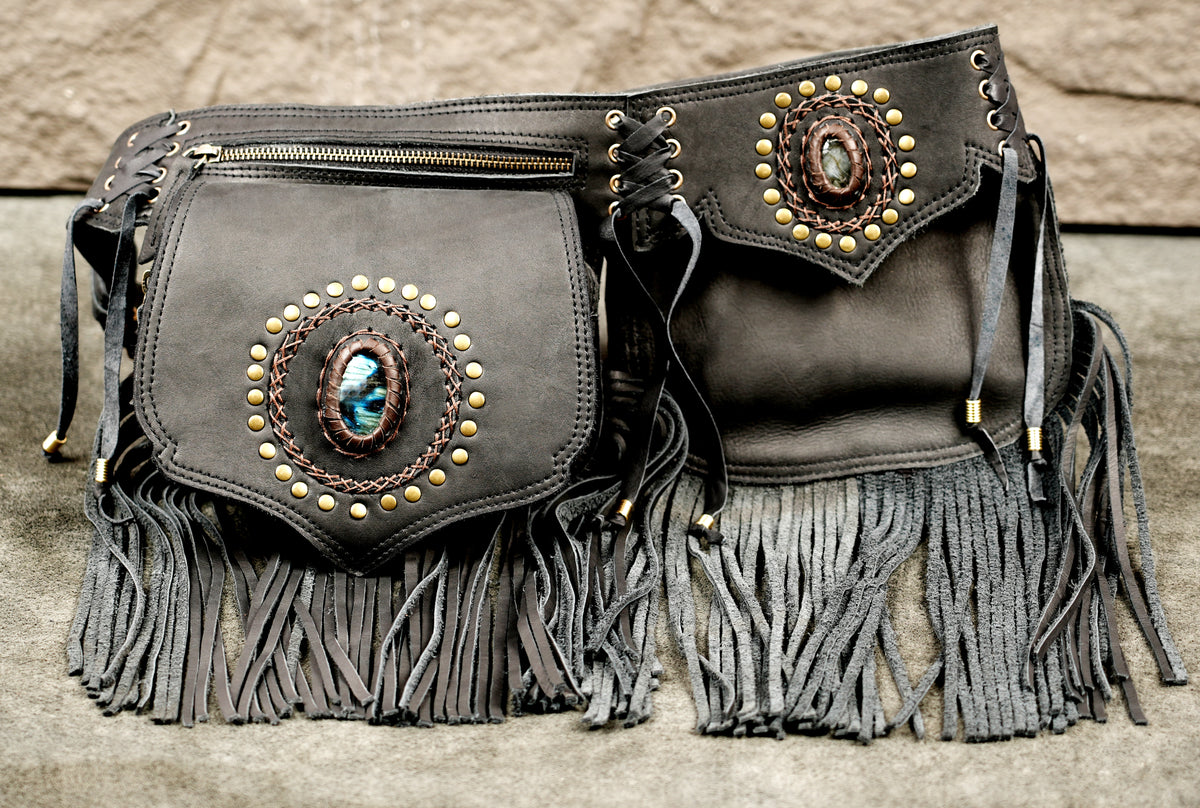 A dark brown leather belt bag with fringe, featuring two front pockets decorated with circular turquoise and gold-tone stone inlays.