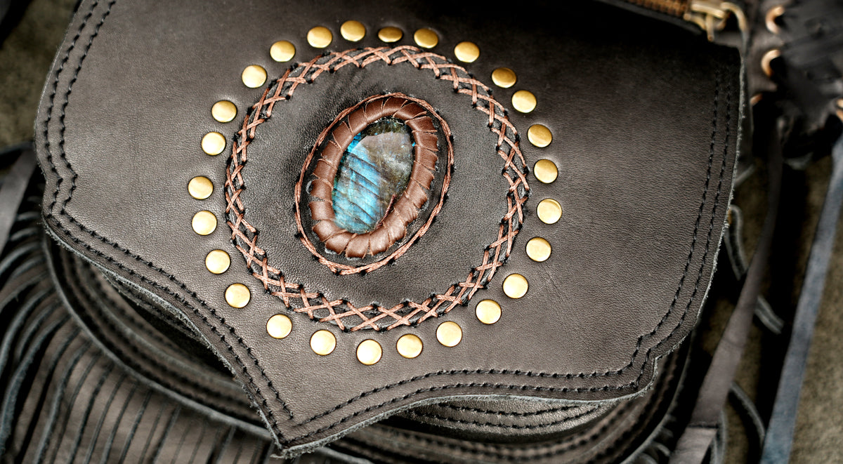 Close-up of a dark brown leather bag featuring a central oval inlay with a blue-green stone.
