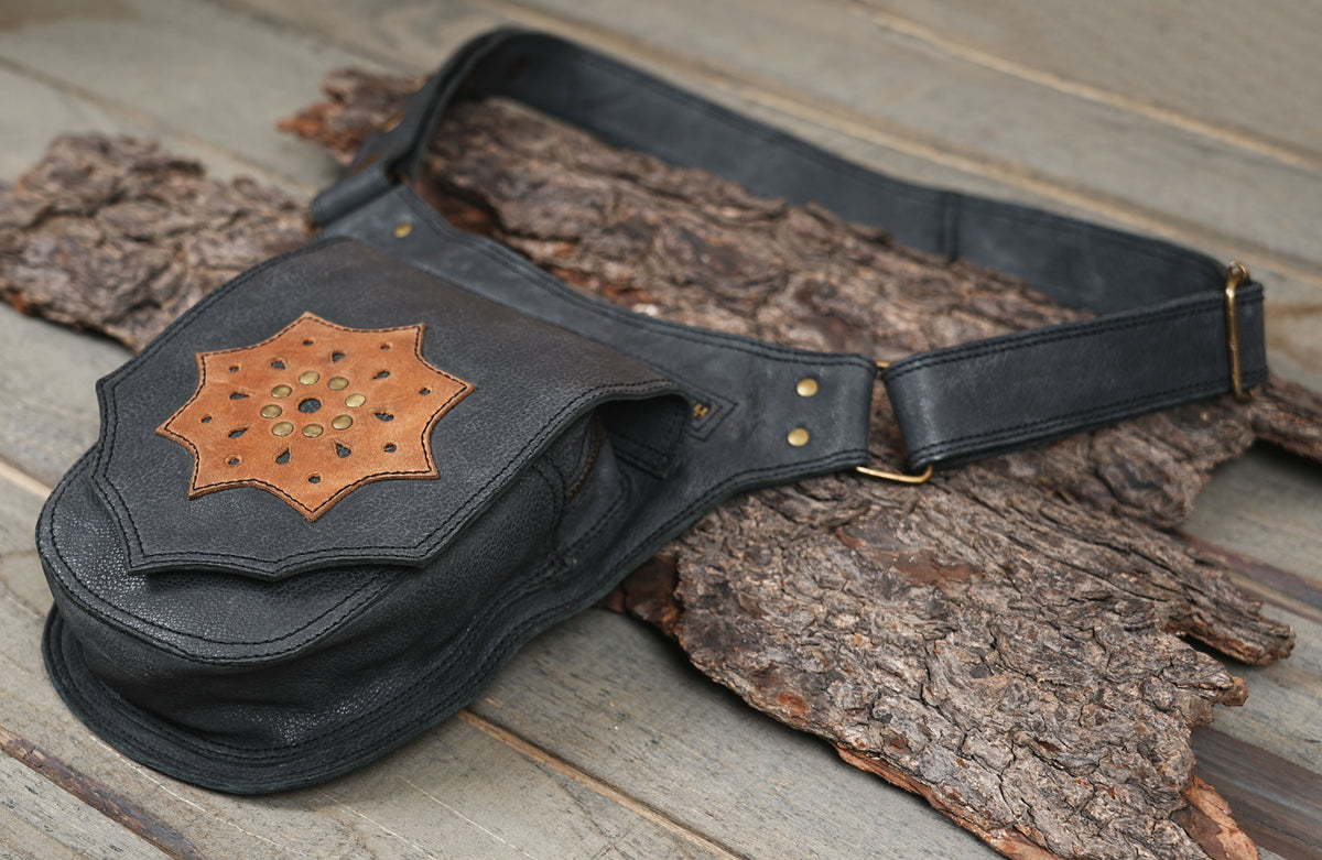 Unisex black leather waist bag with brass hardware on tree bark background