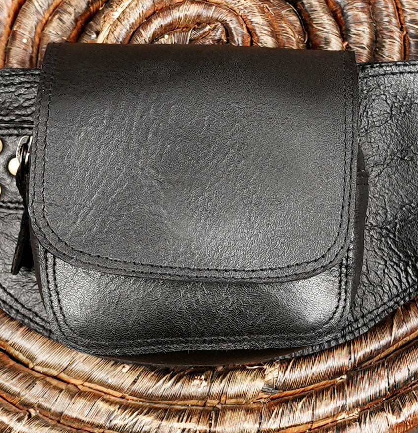 A close-up of a black leather pouch or small bag with a flap closure, placed on a woven straw or rattan surface.