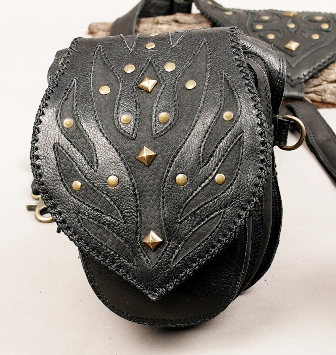 Black leather crossbody bag with a decorative flap featuring stitched leaf-like patterns and brass studs.