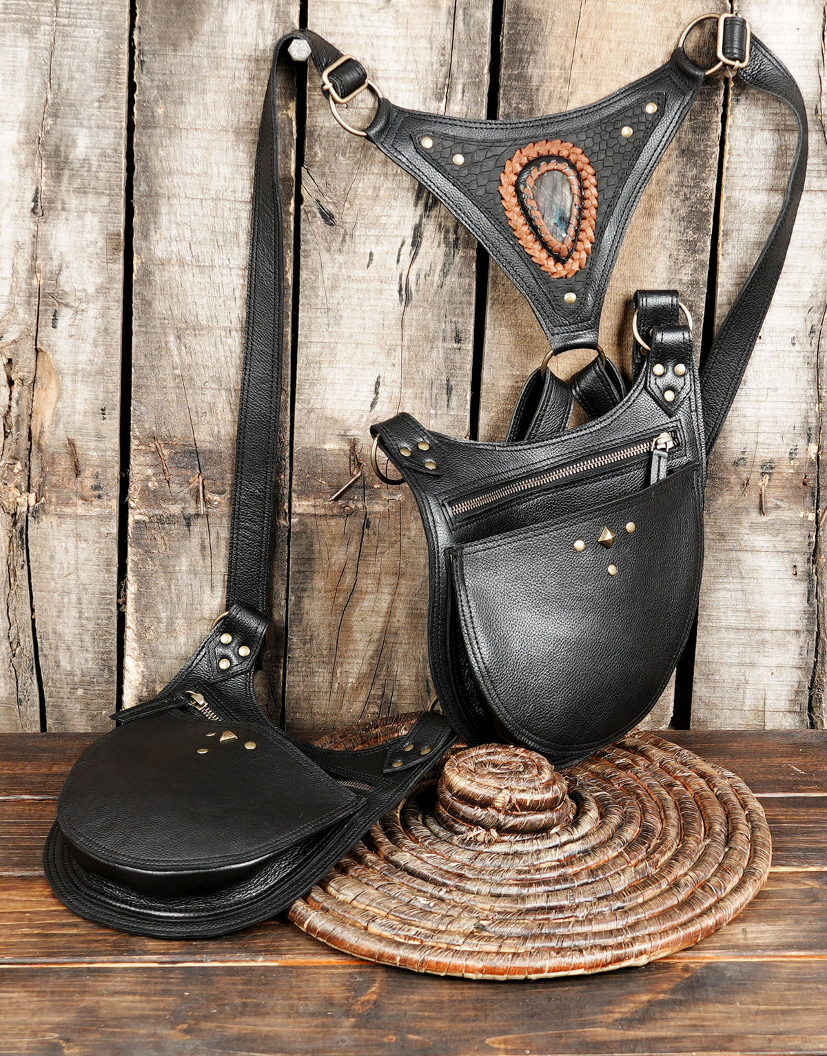 A black leather saddle-style crossbody bag with a matching adjustable shoulder harness and a separate detachable saddle pad.