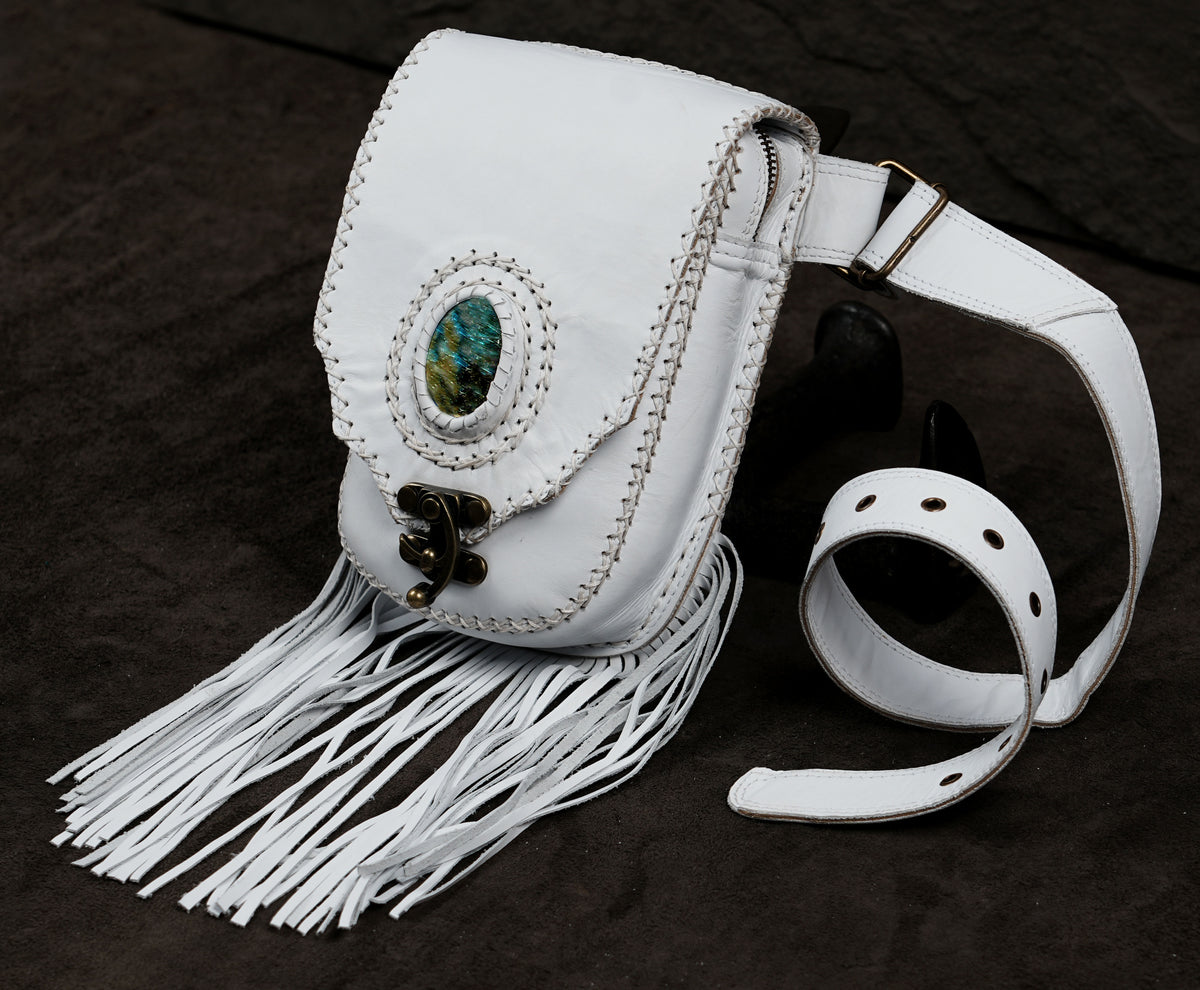 A white leather crossbody bag with fringe detailing, a turquoise stone accent, and a matching white leather strap.