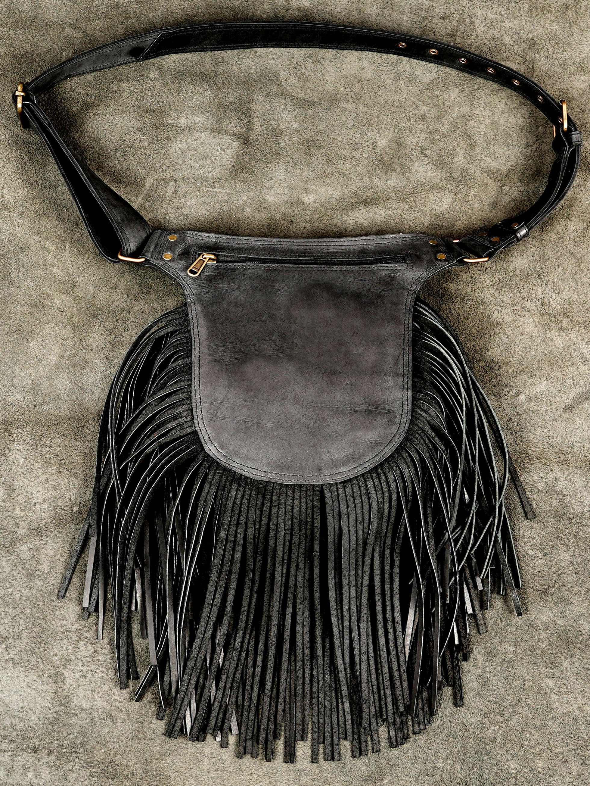 Handcrafted leather waist bag with fringe, close up on stone