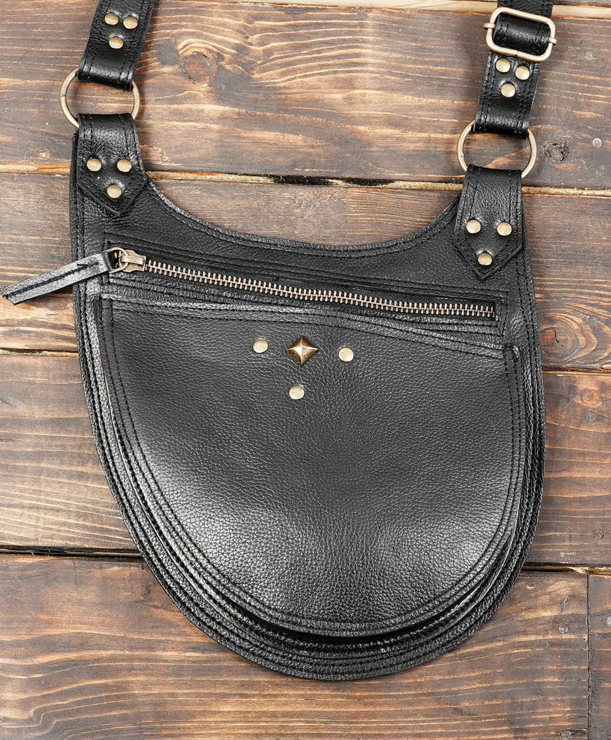 Black leather crescent-shaped shoulder bag with gold-tone hardware, a front zip pocket, and decorative studs.