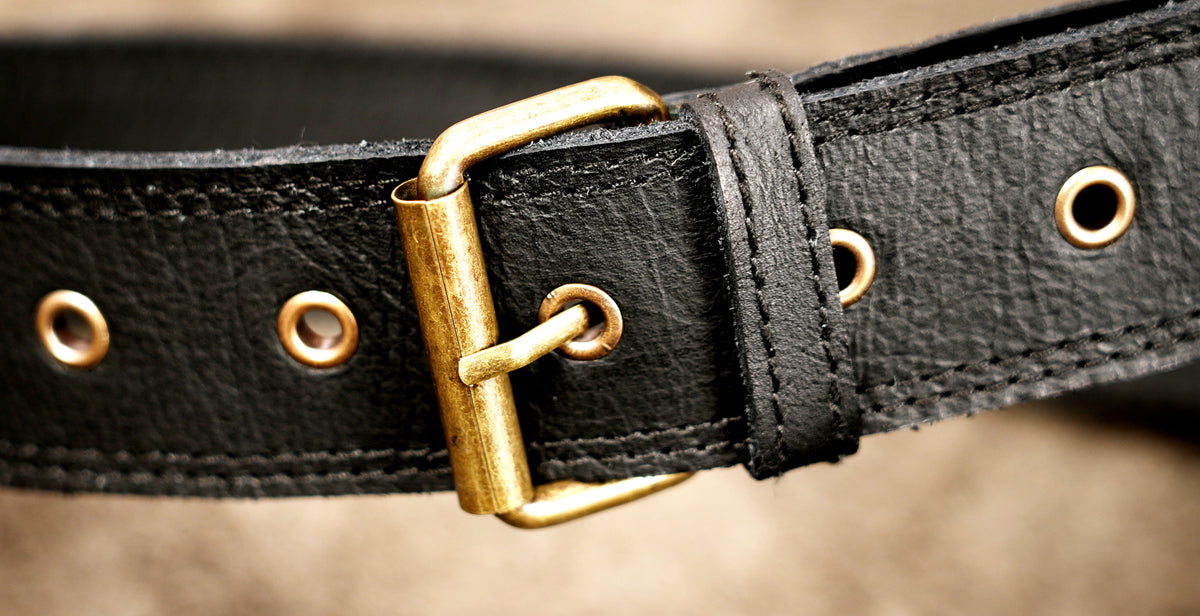Close-up of a black leather belt with a brass buckle and metal eyelets.