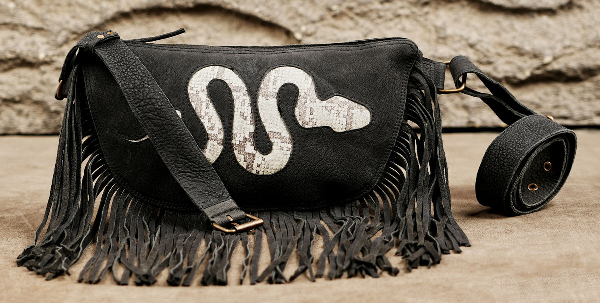 Black boho belt bag with long fringe detailing and white snake motif for music festivals.
