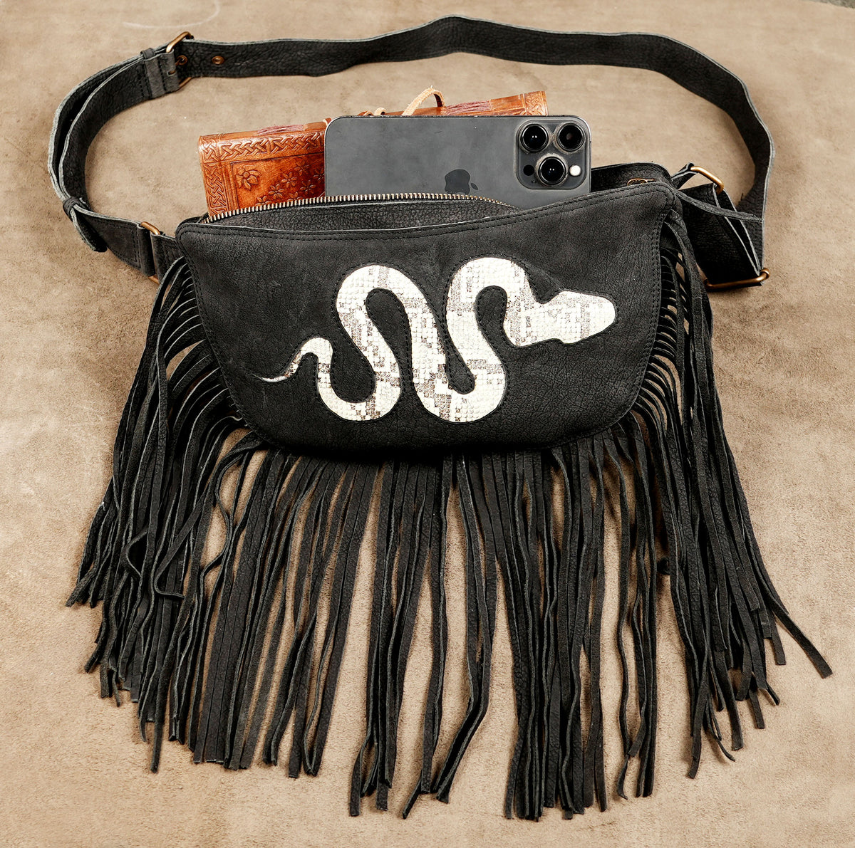 Black cowboy-inspired belt bag with long fringe and white snake decoration for festivals.